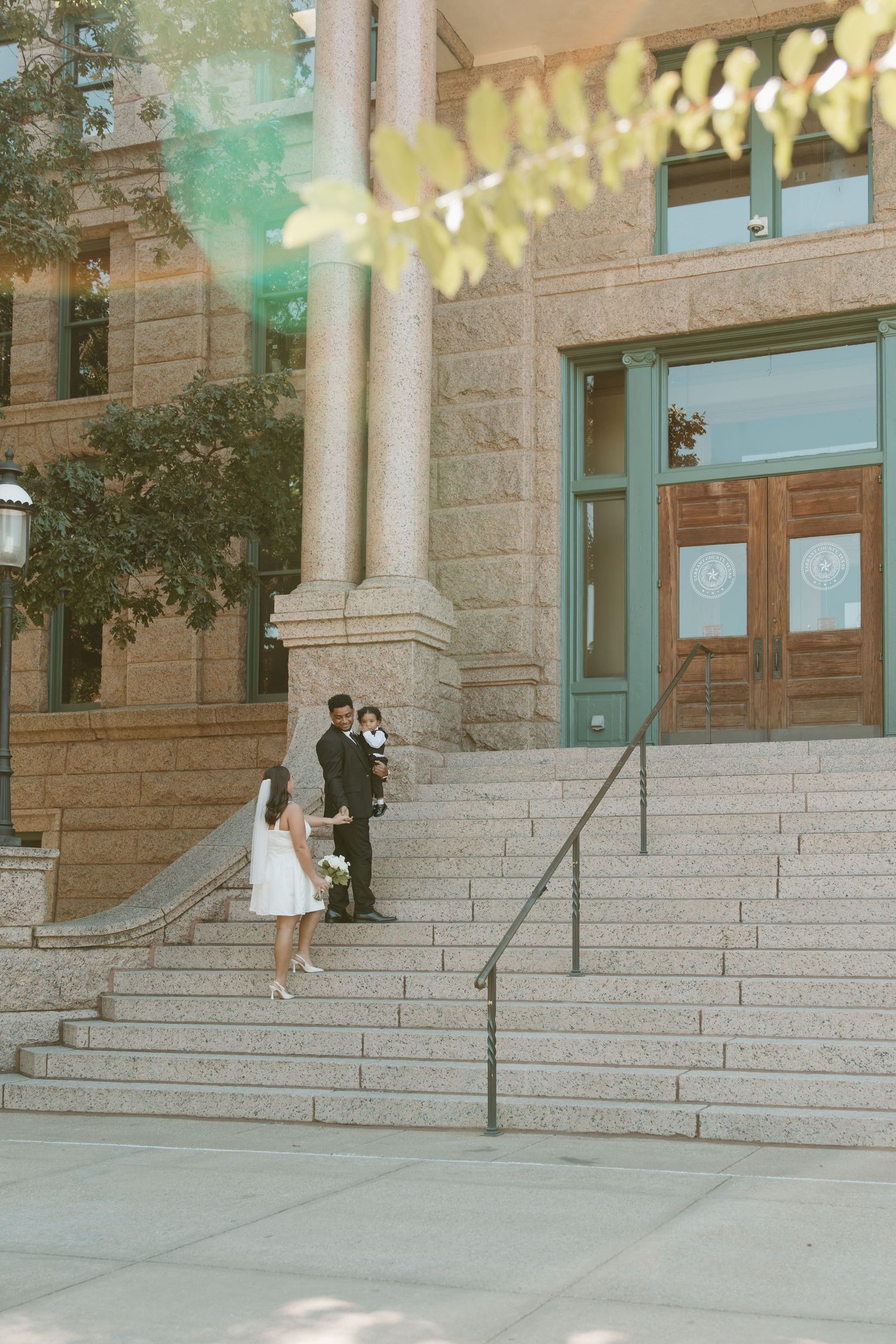 A couple stands on stone steps of a grand historic building with decorative lights strung above. Wedding Photographer DFW