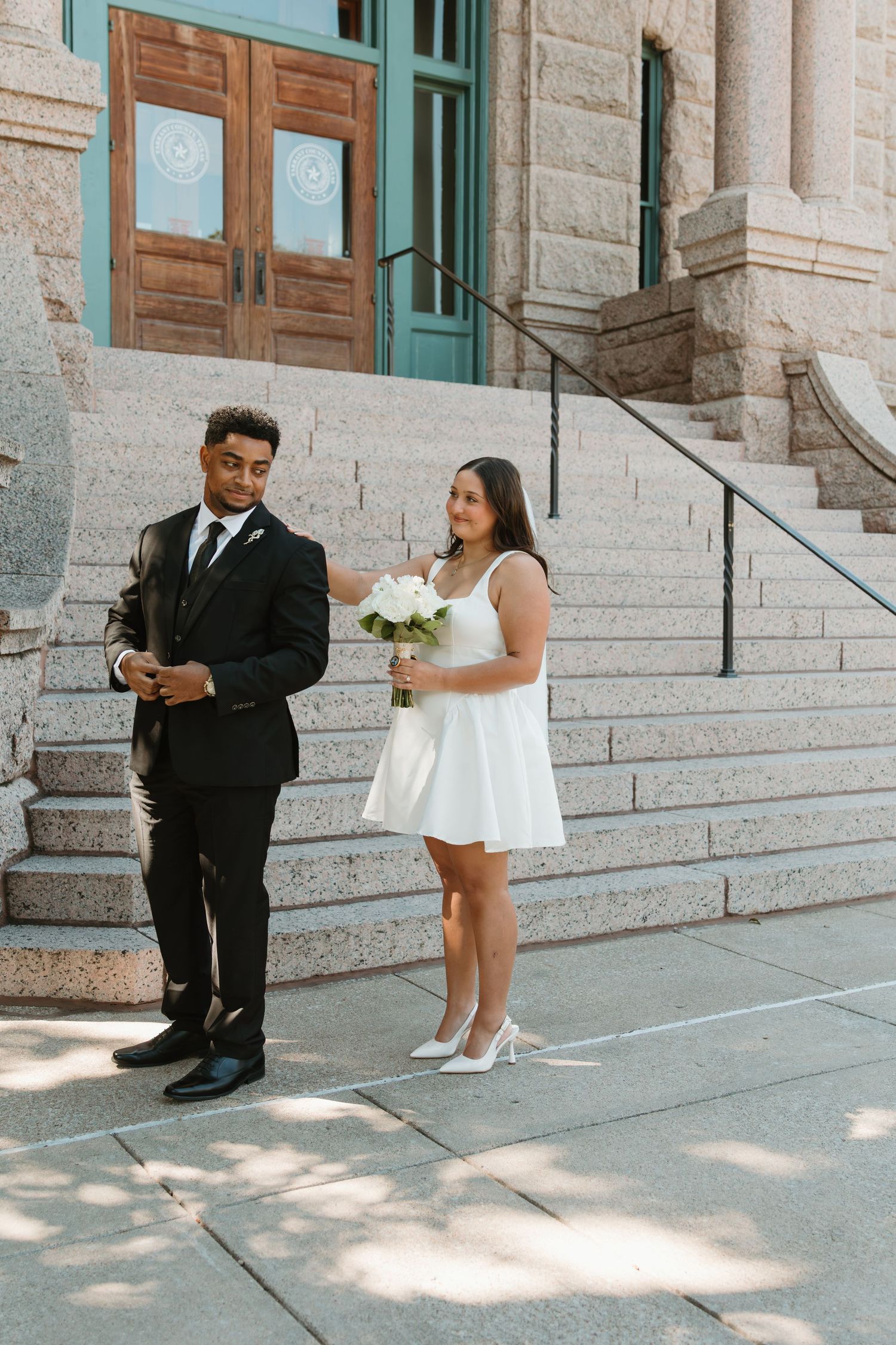 A couple in formal attire shares an intimate moment on stone steps outside a historic building. Wedding Photographer DFW