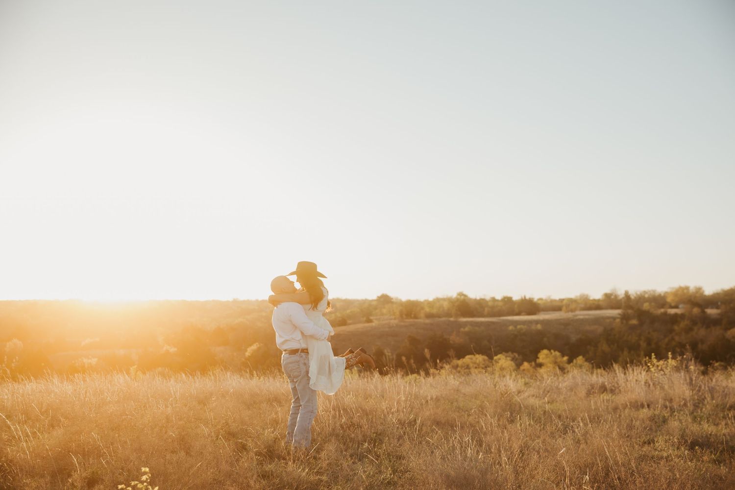 Couple embracing in golden sunlit field at sunset, romantic outdoor portrait in open countryside meadow.