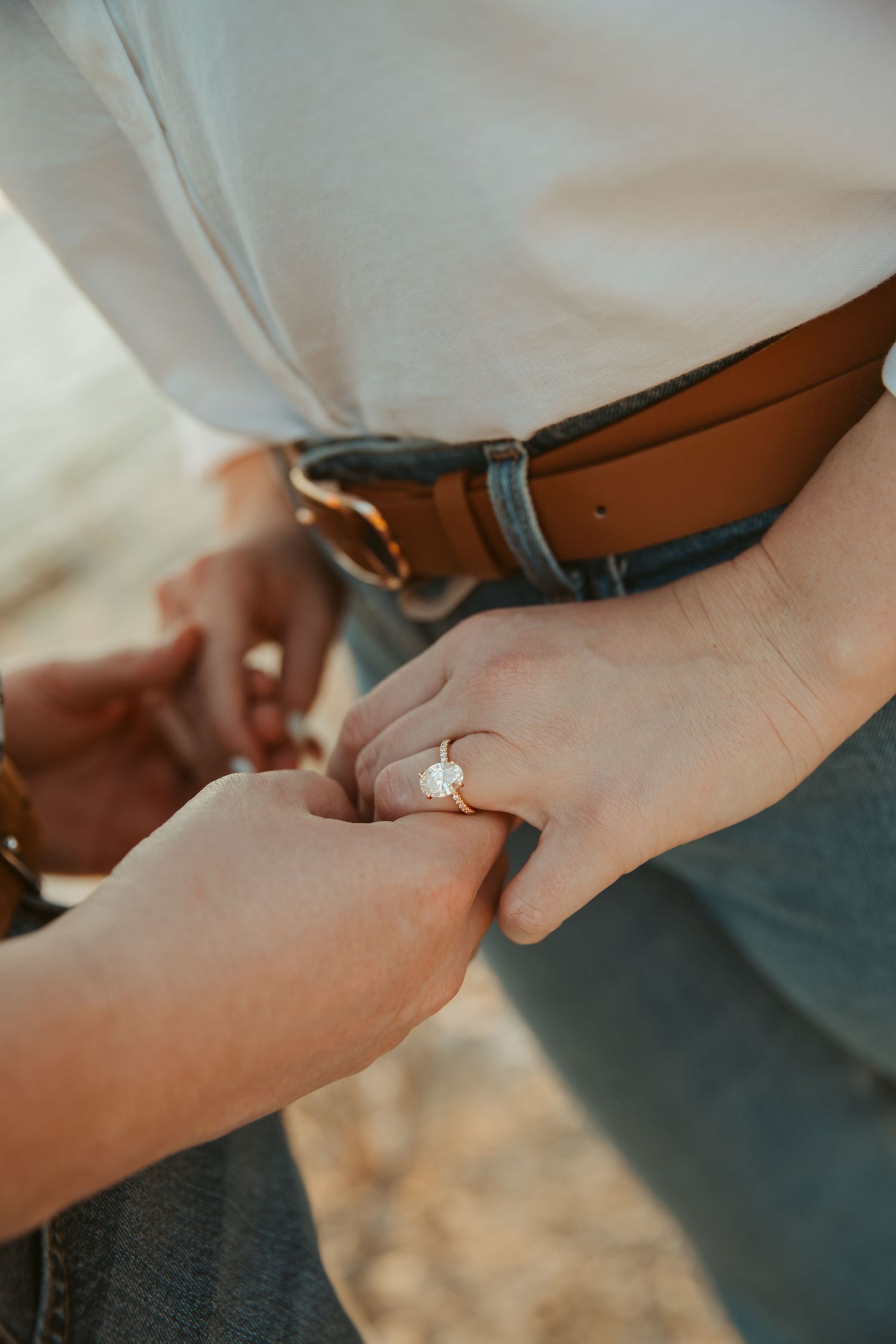 Close-up of woman's hand wearing oval diamond engagement ring while holding partner's hand.