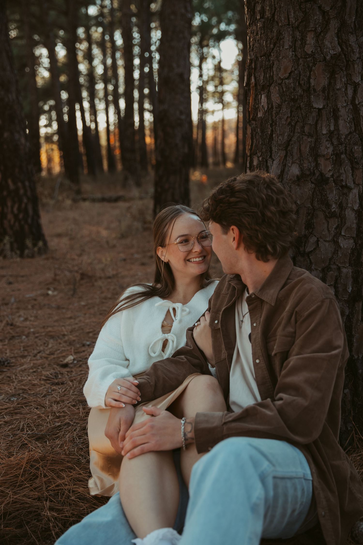 Couple sharing intimate moments while sitting among pine trees at sunset. engagement photos Fort Worth