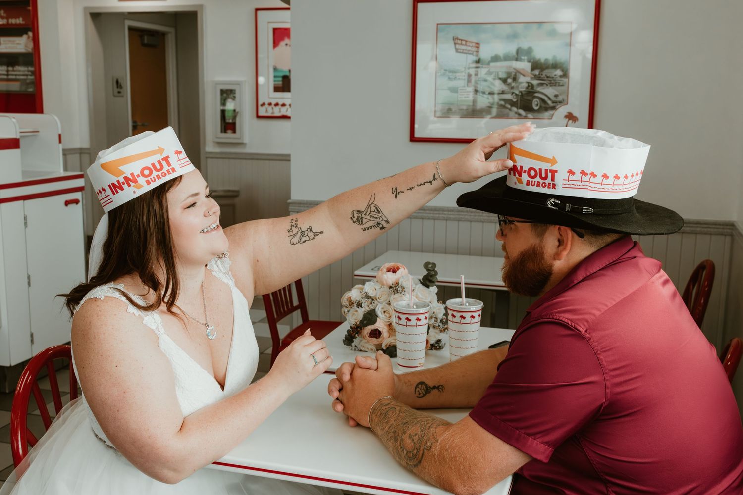 A couple wearing paper hats shares a playful moment at a diner counter.