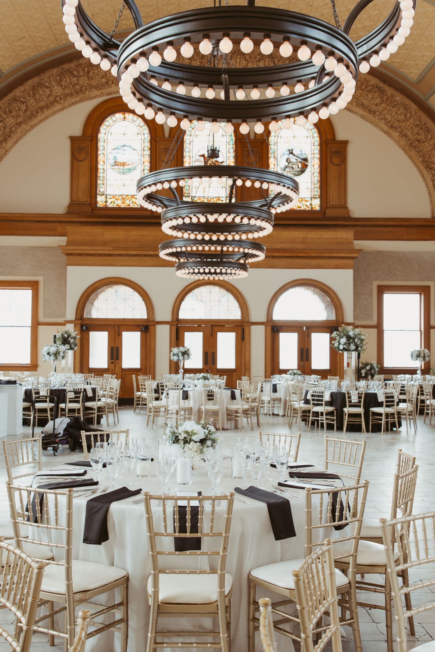 Elegant wedding venue with circular chandeliers and round dining tables set in a grand room with arched details.