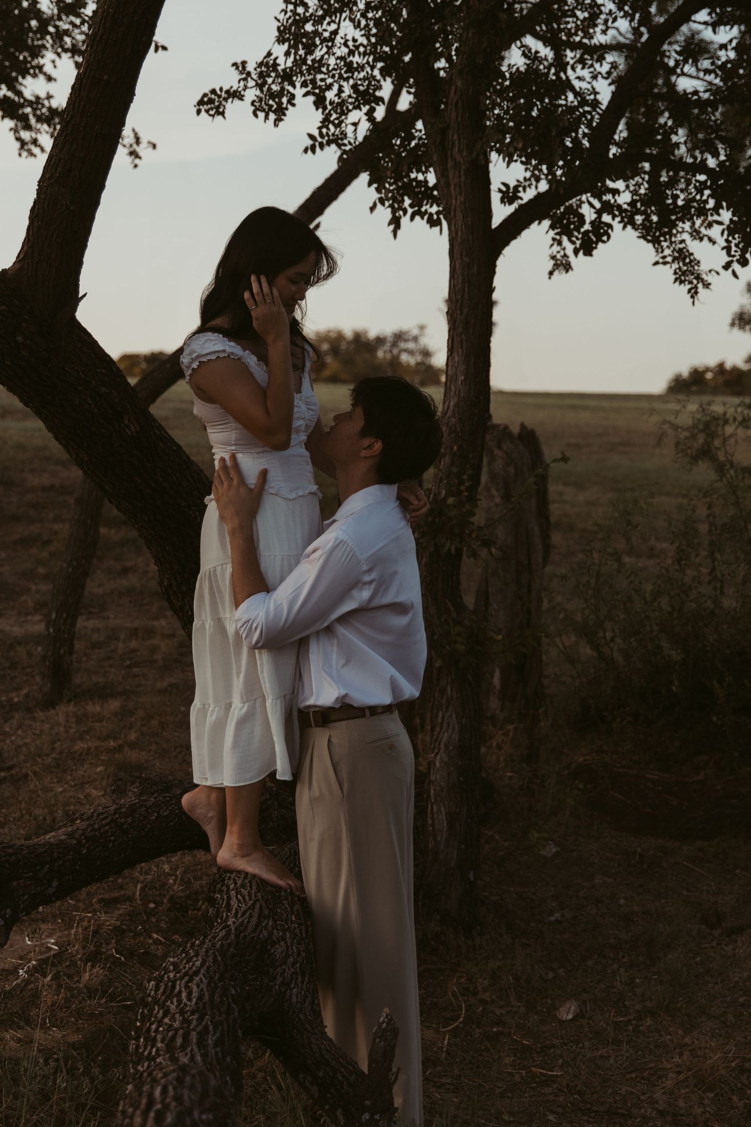 A romantic sunset moment captured between two people by a tree in a rural setting.