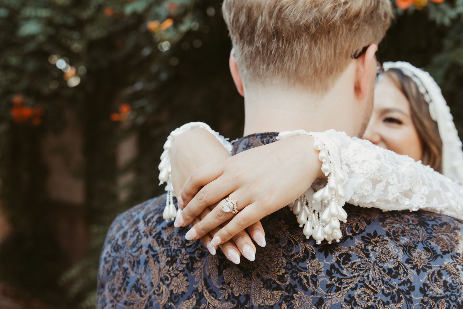 Close-up shot showing embracing couple with lace details and autumn foliage in background.