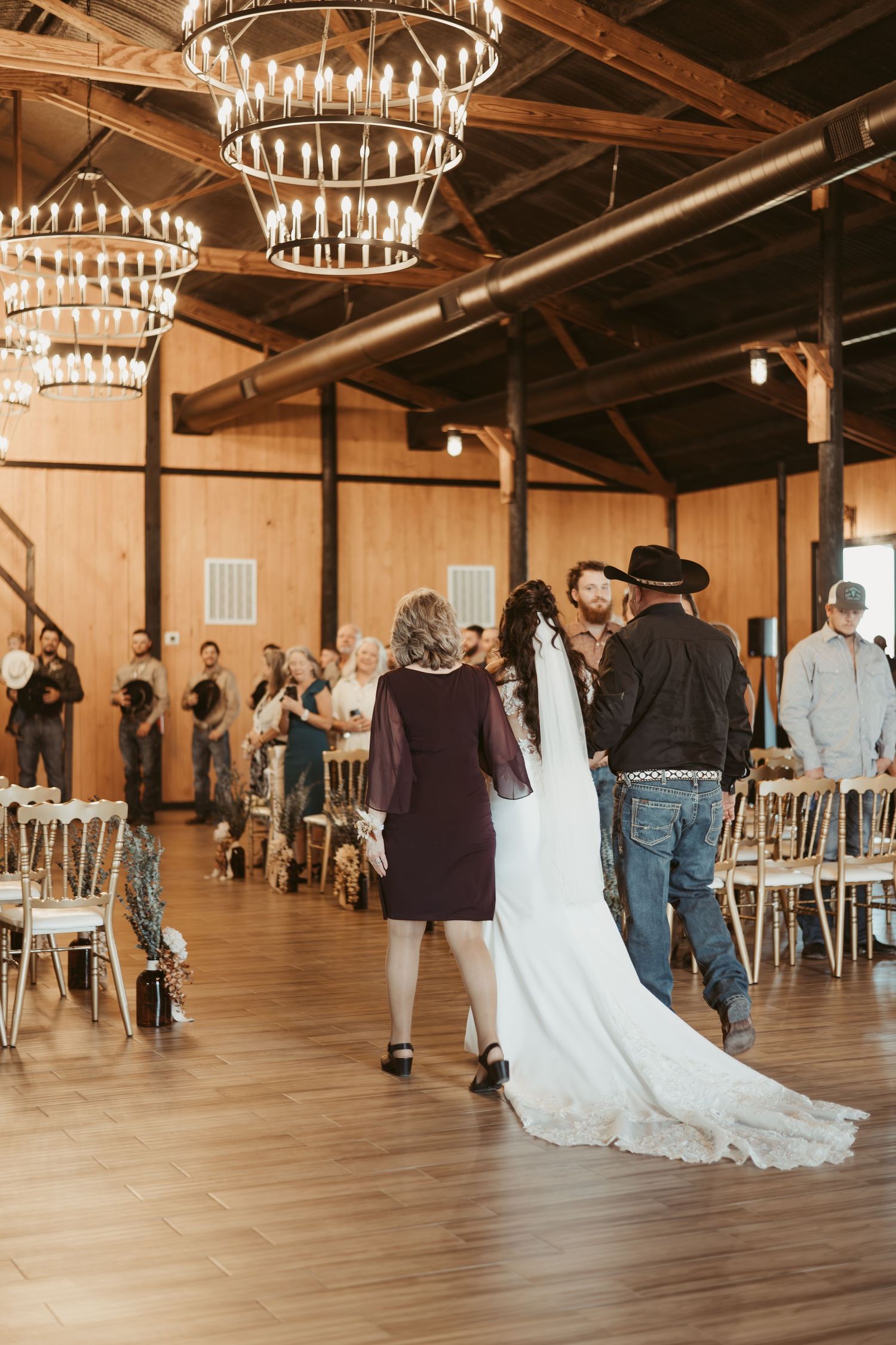 A spacious rustic wedding venue with wooden floors, elegant chandeliers, and guests mingling during a reception. Wedding photographer DFW