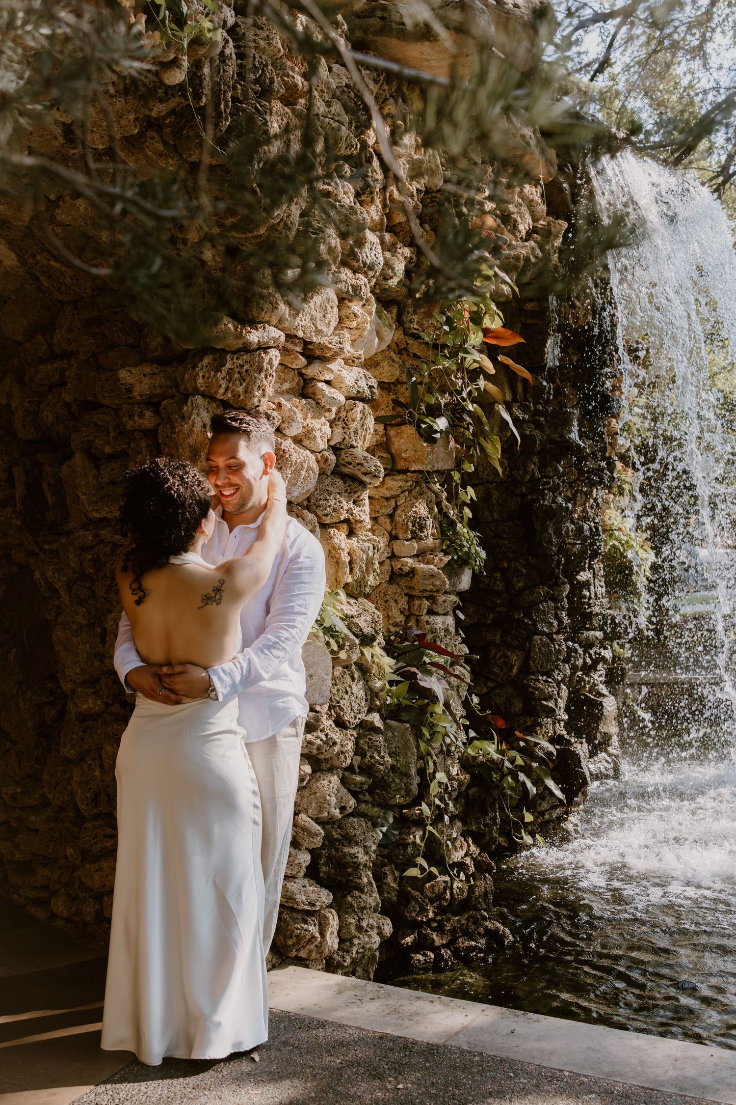 A couple shares intimate moments by a cascading waterfall against a stone wall backdrop.