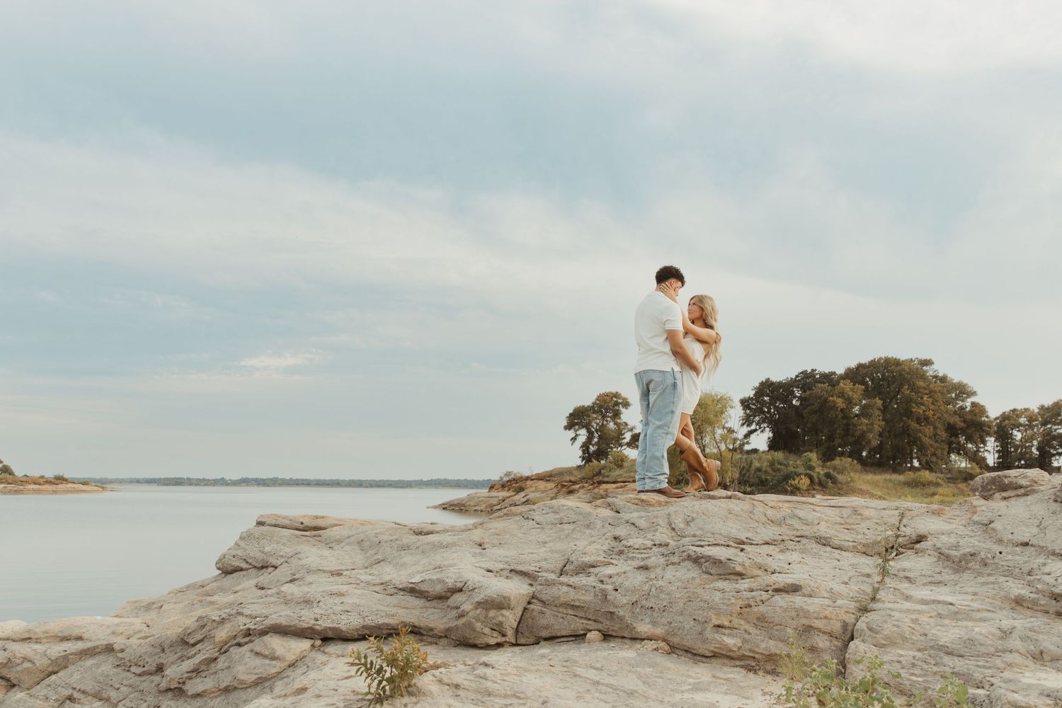A couple sits together on a rocky coastal cliff overlooking the ocean during golden hour.