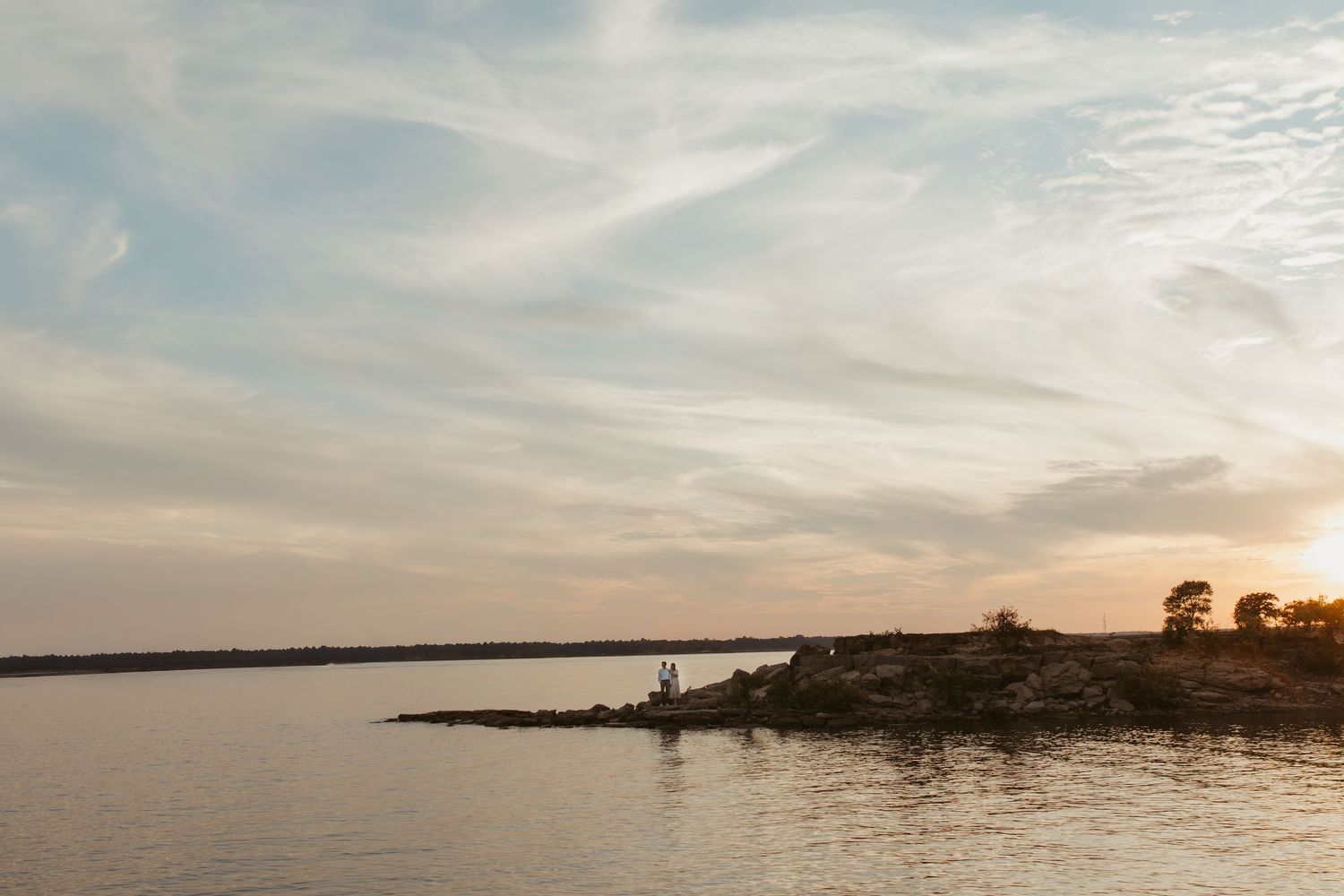 Scenic sunset view of a rocky coastline with silhouetted trees and calm waters.