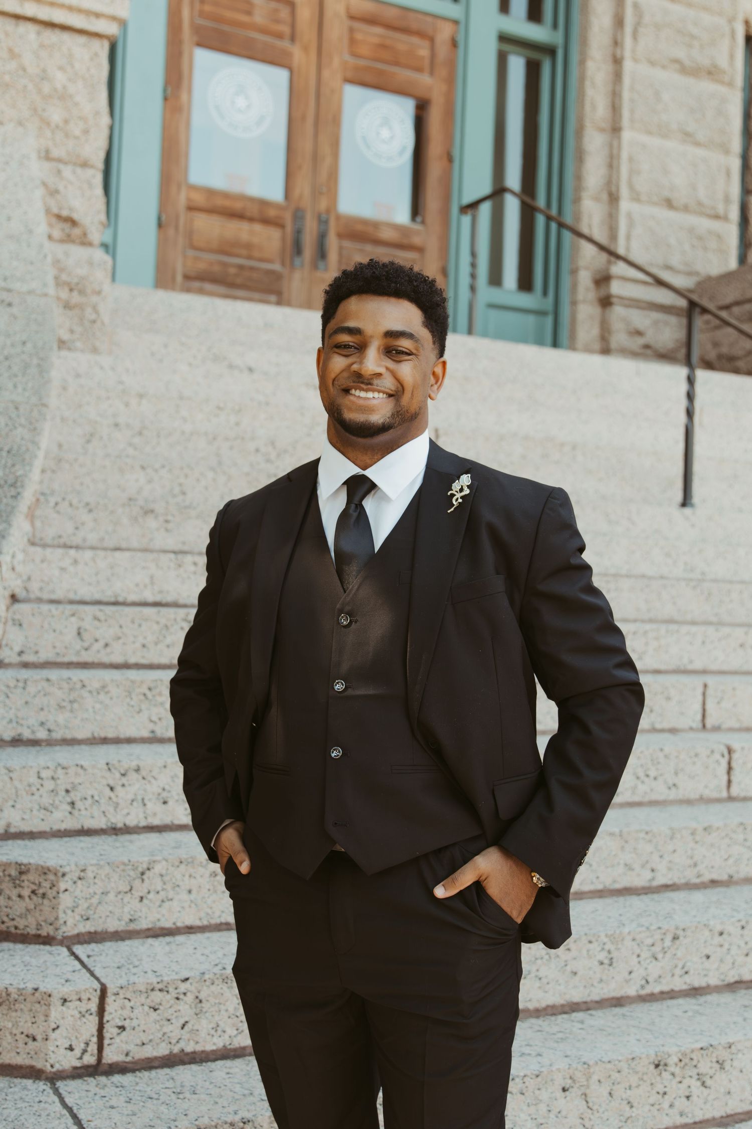 A person in a black suit stands confidently on stone steps of a historic building. Wedding Photographer DFW