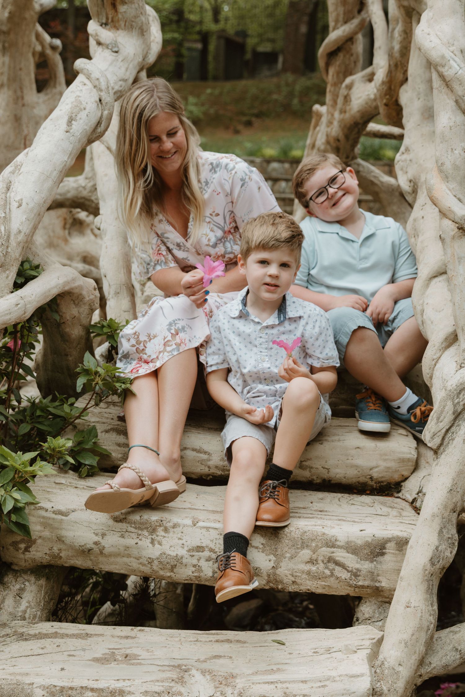 Family sitting together on rustic driftwood logs in an outdoor setting wearing casual spring clothing.