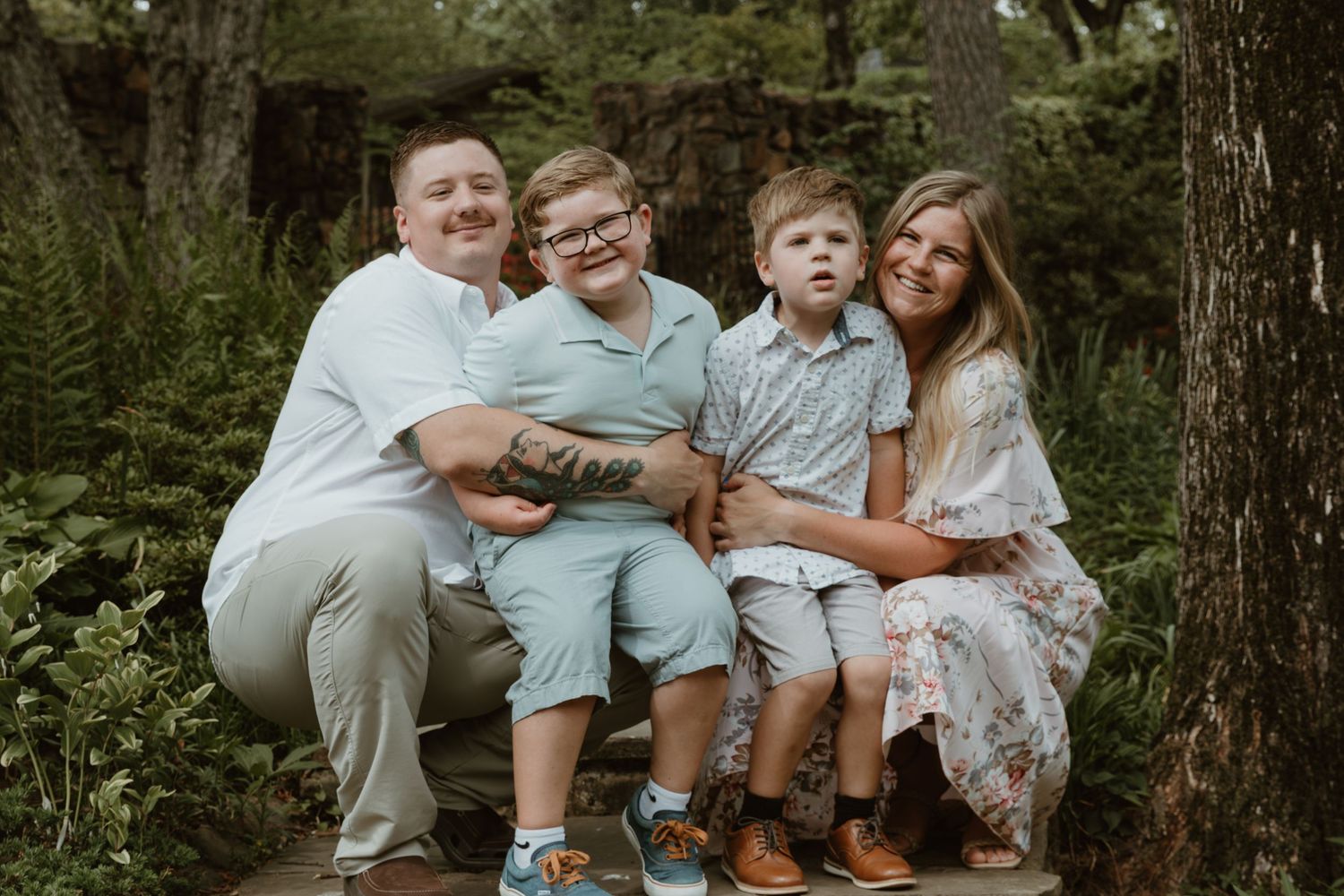 A family group sitting together on a wooden bench surrounded by lush green foliage in a forest setting.