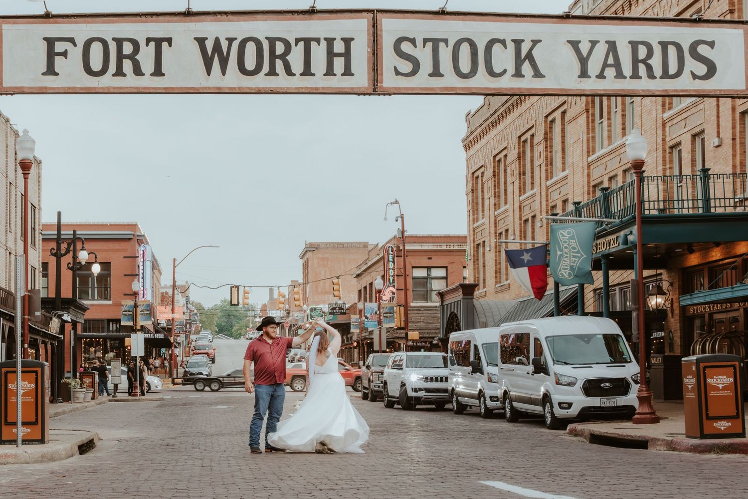 Wedding couple posing under Fort Worth Stock Yards sign on historic street.