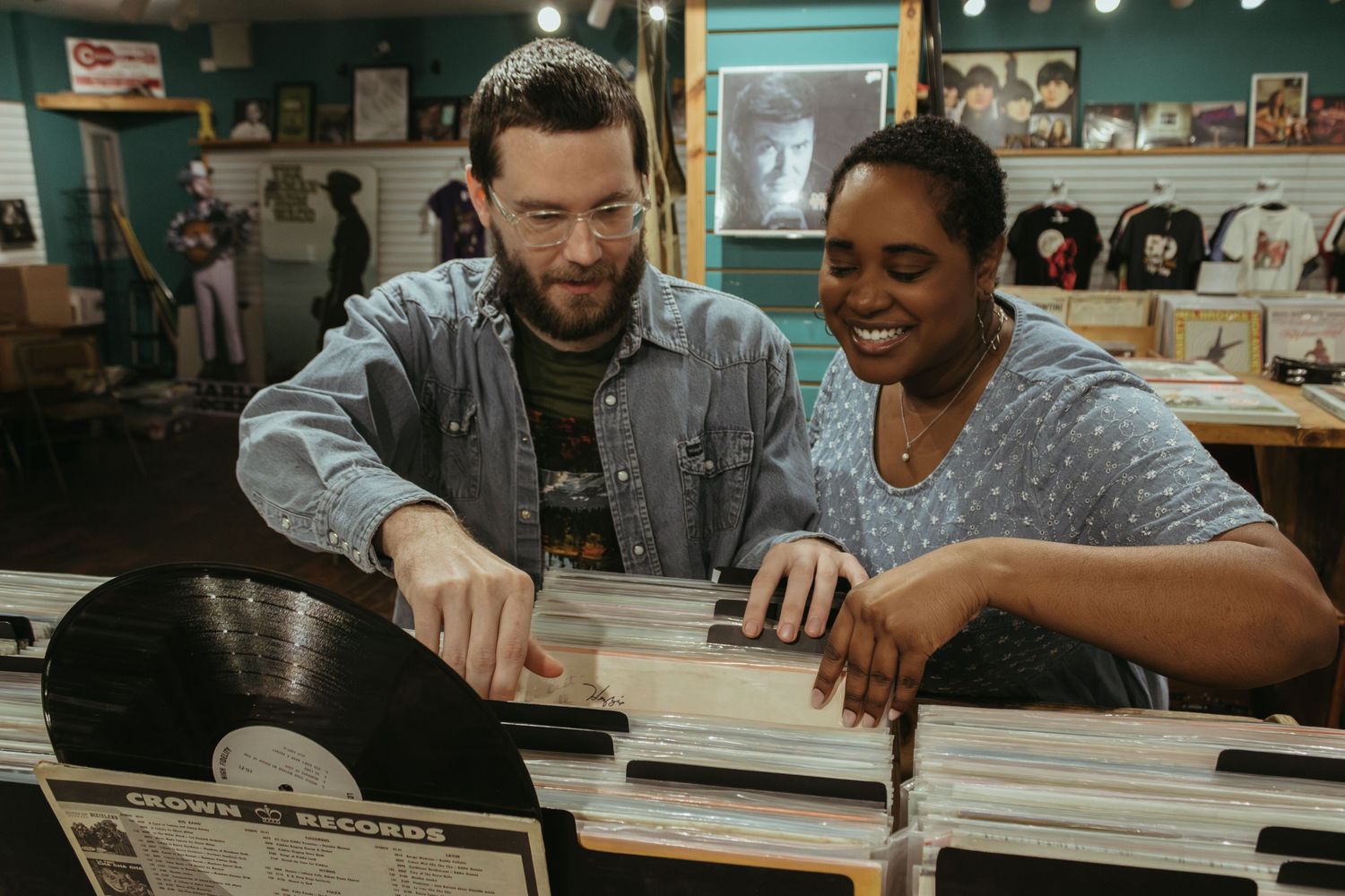 Two people browse through vinyl records and music albums together at a record store with green walls.