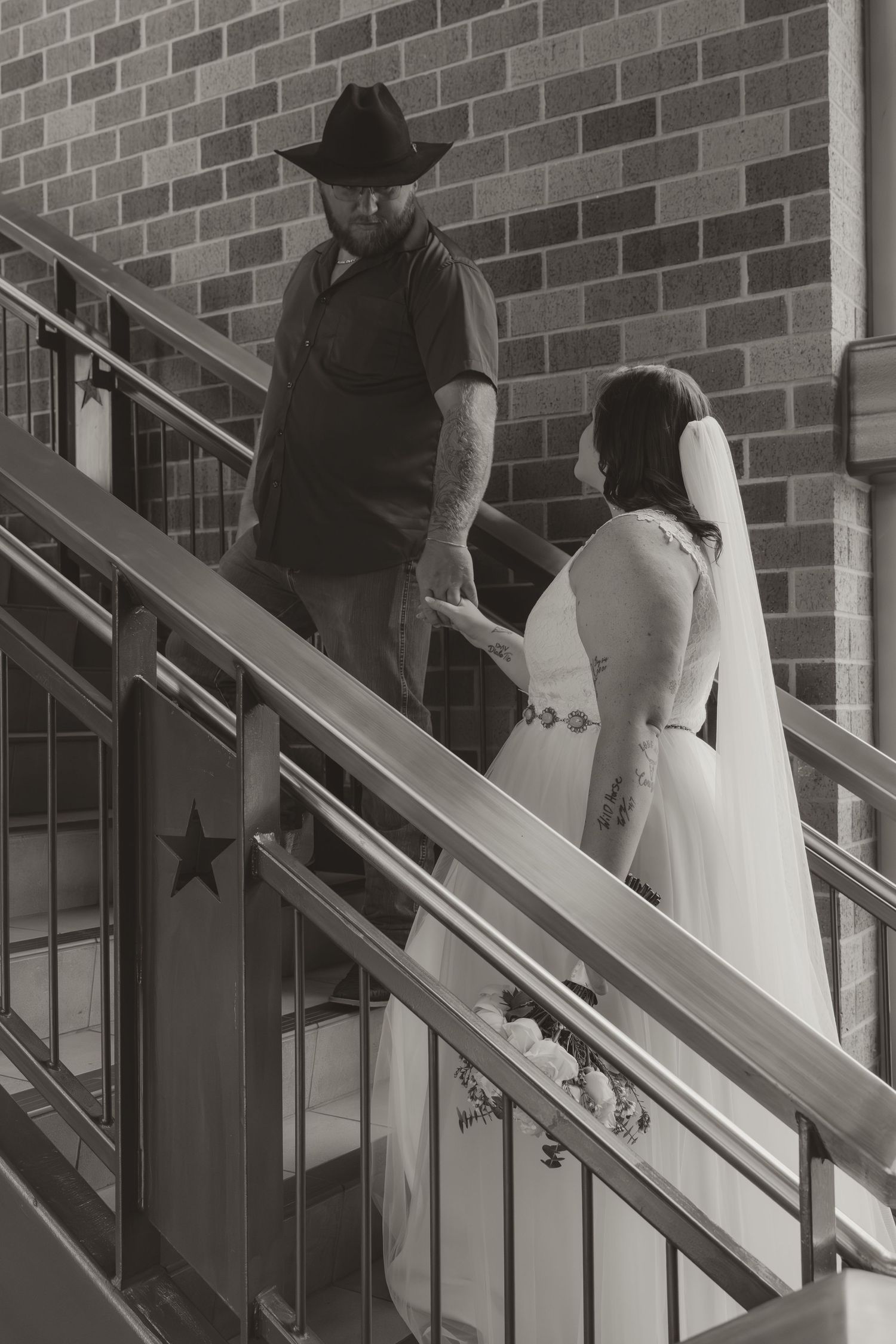 A black and white wedding photo on staircase with rustic brick wall backdrop.