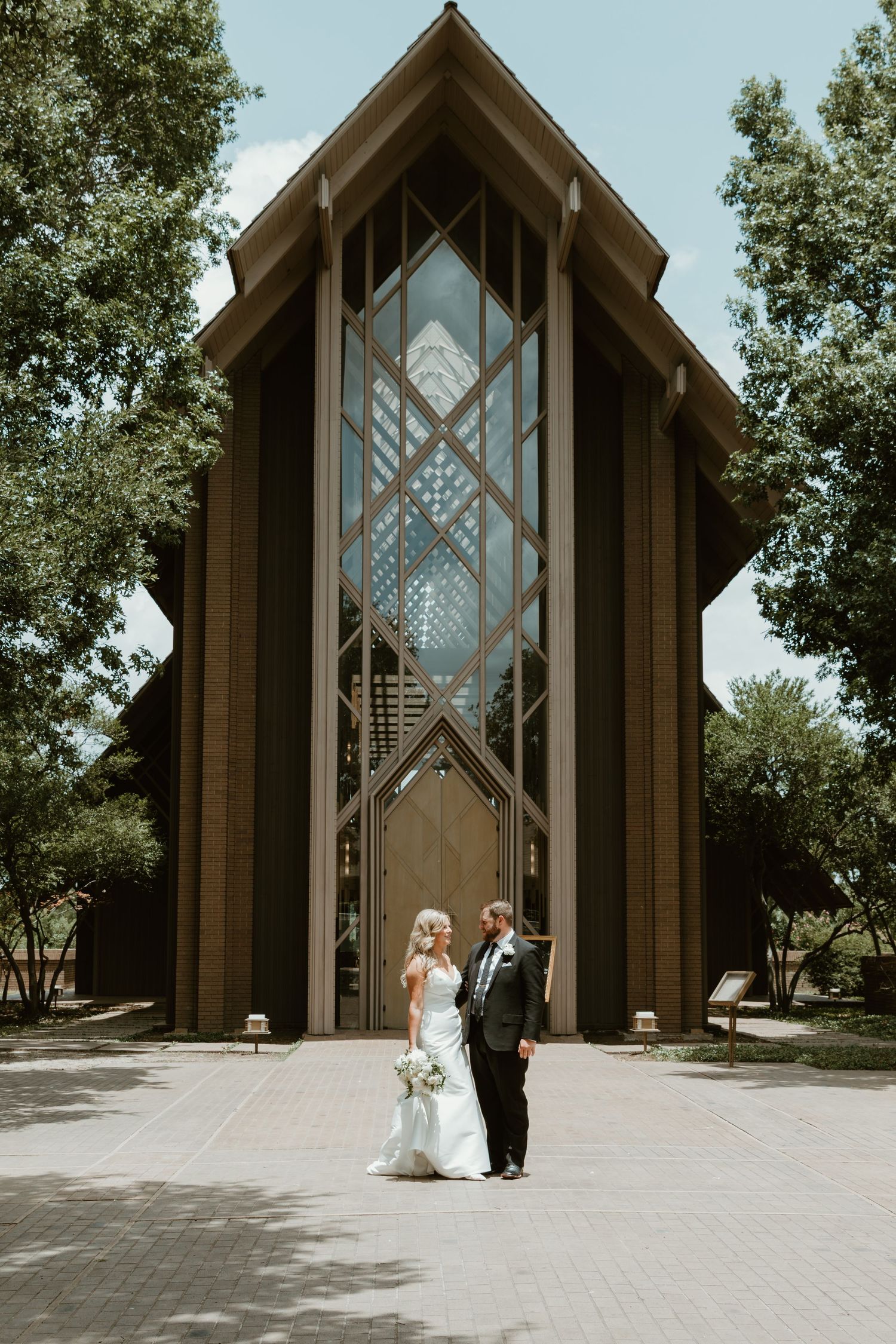 A bride and groom walk away from a modern glass and wood chapel in five different progression shots.