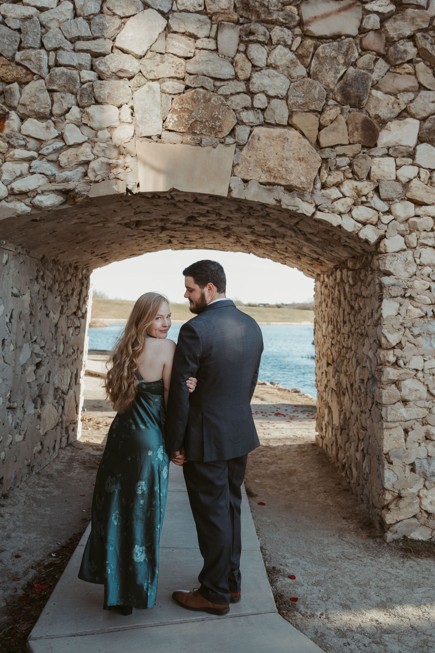 A couple shares an intimate moment under a stone archway overlooking the ocean during a photo session.