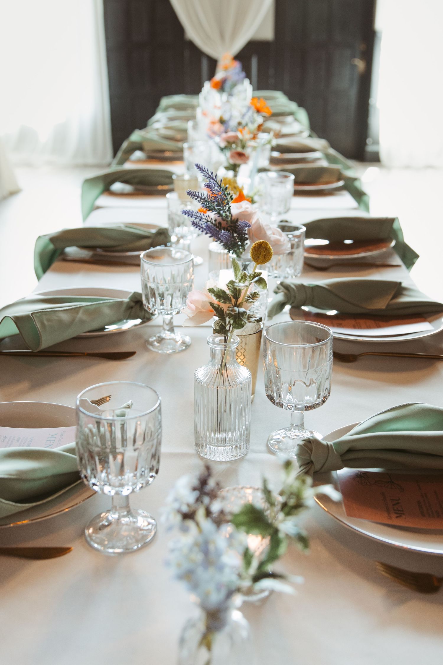 Elegant table settings with dark plates, crystal glasses, and delicate floral arrangements in muted tones.