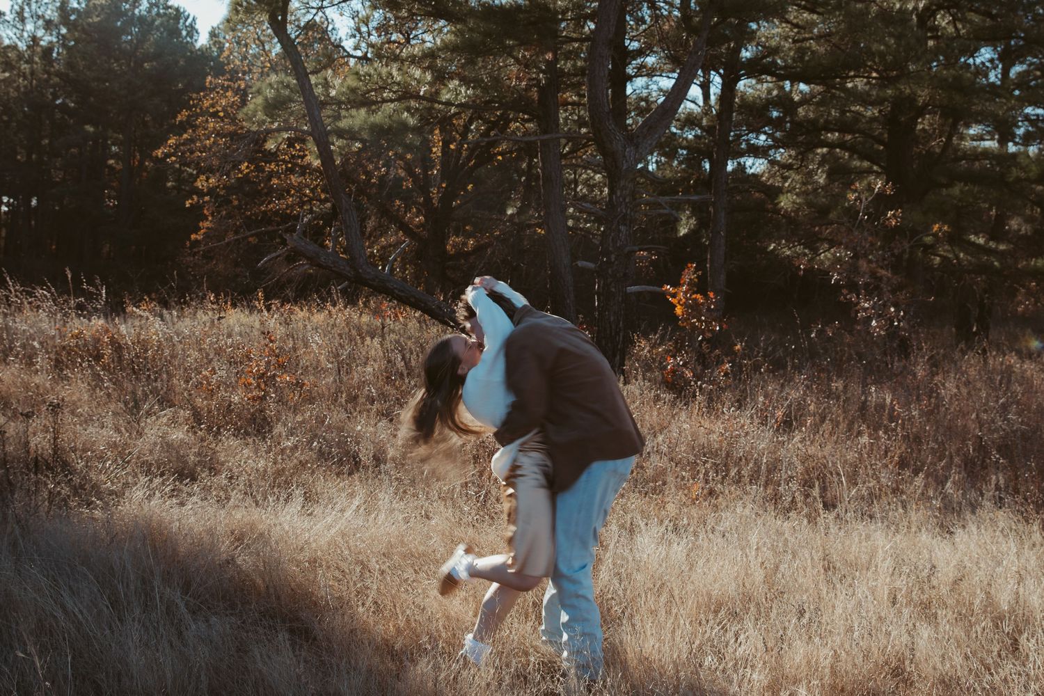 A person in casual attire walks through a golden autumn field with tall dried grass and trees in the background. engagement photos DFW