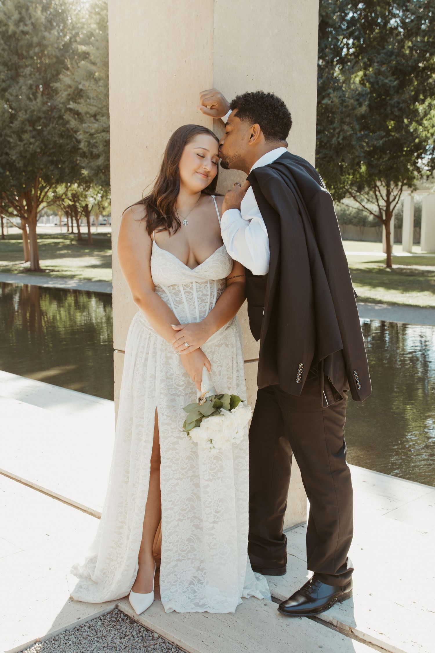 Wedding couple shares intimate moments by a reflecting pool with natural lighting and architectural backdrop. Wedding Photographer DFW