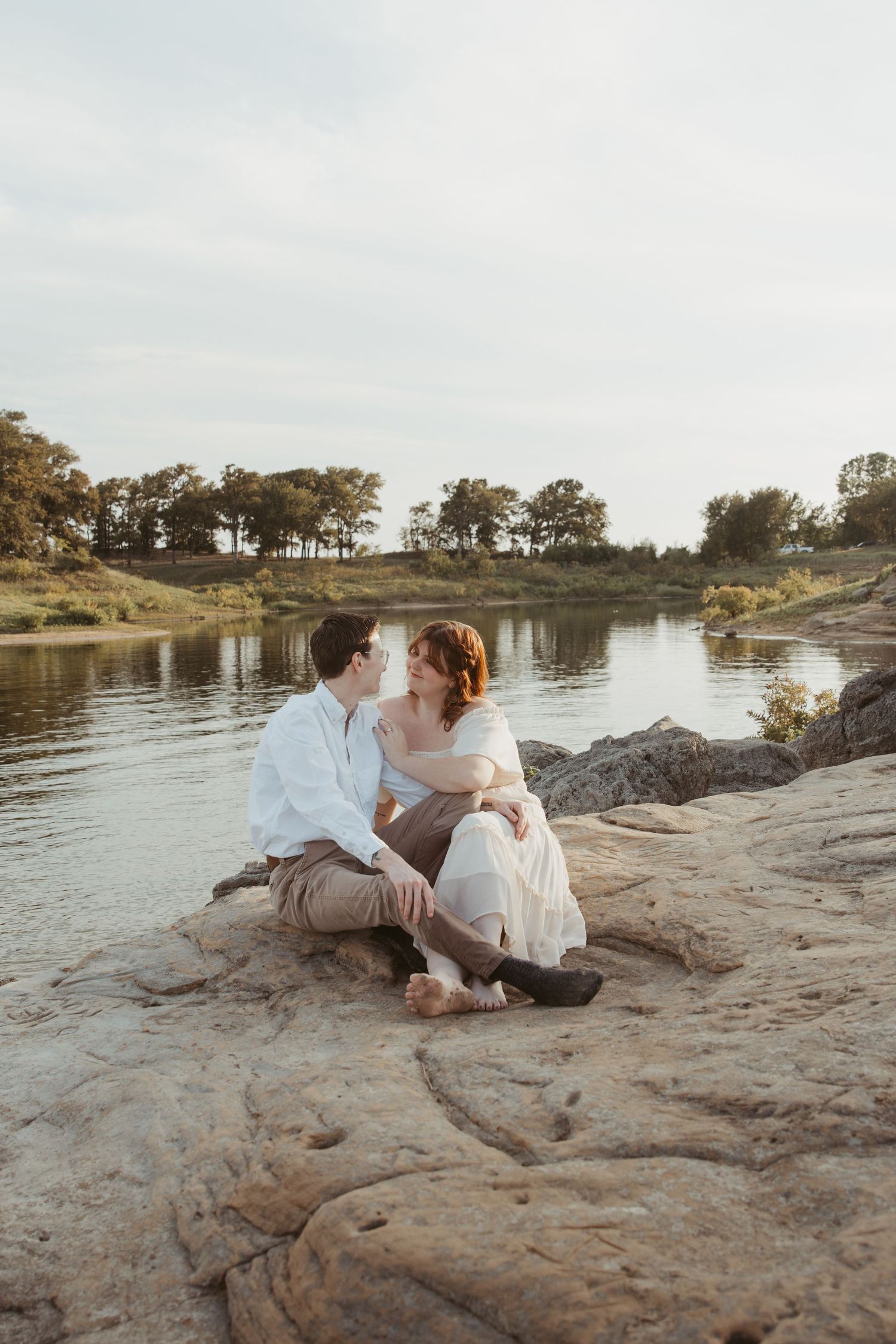 A romantic lakeside photoshoot on rocky terrain at sunset with white and grey attire.