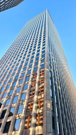 Low-angle view looking up at a tall glass and steel skyscraper against a clear blue sky.