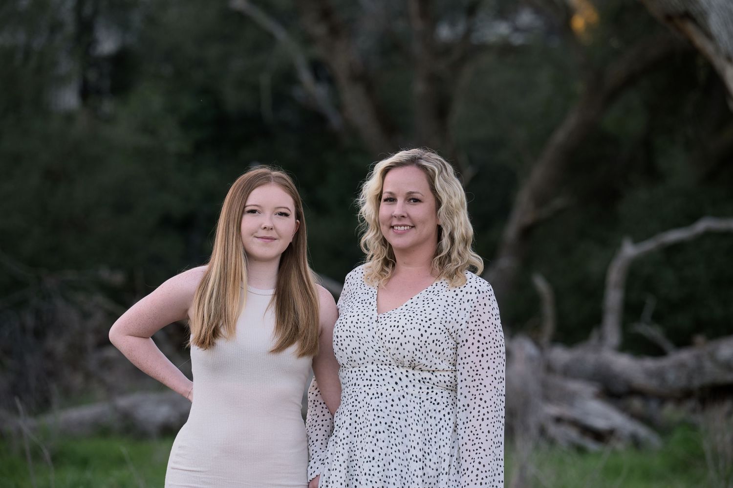 Two women pose together smiling in a natural outdoor setting at dusk.