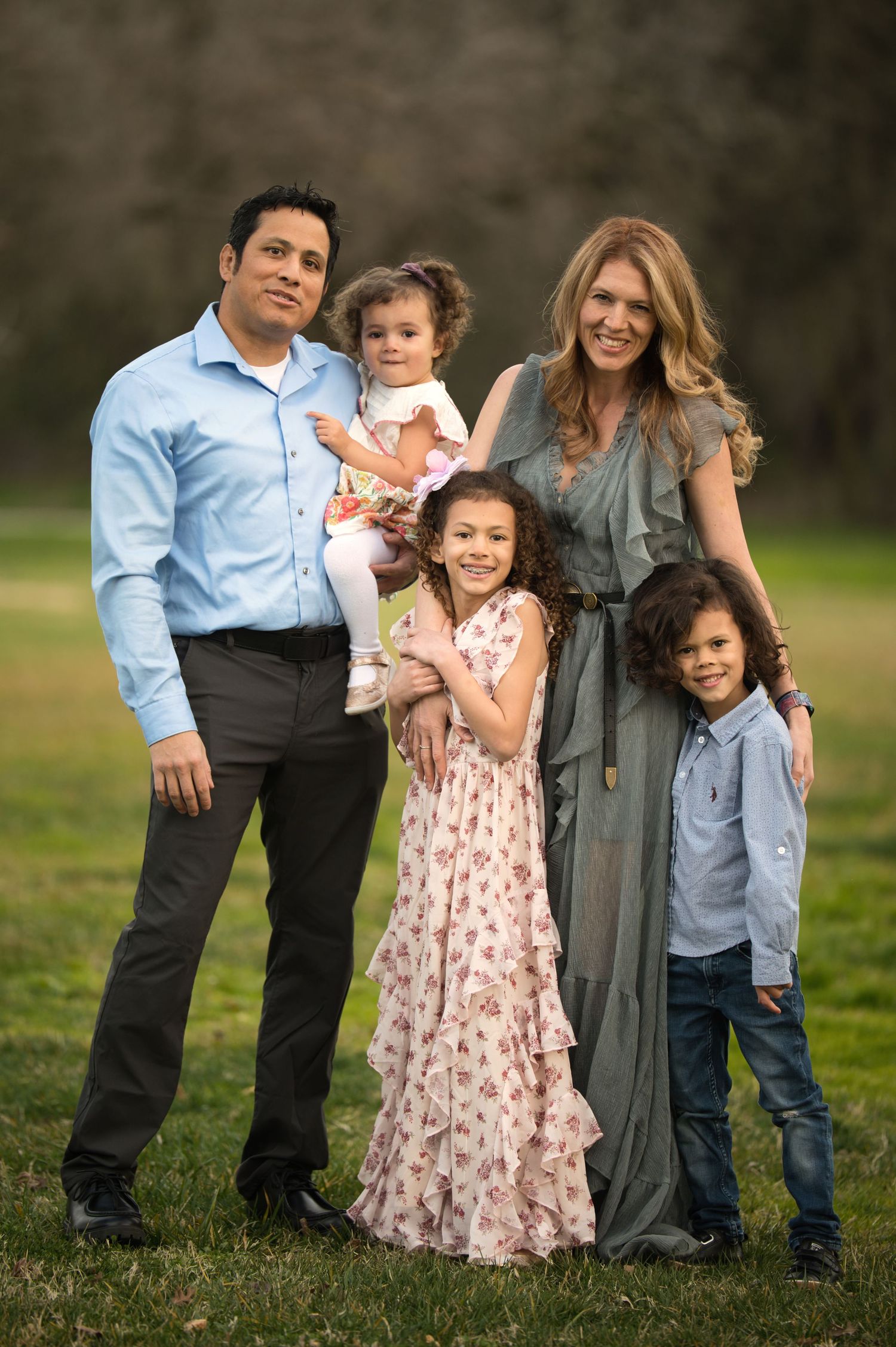 Happy family of five posing together in green park during outdoor photo session.