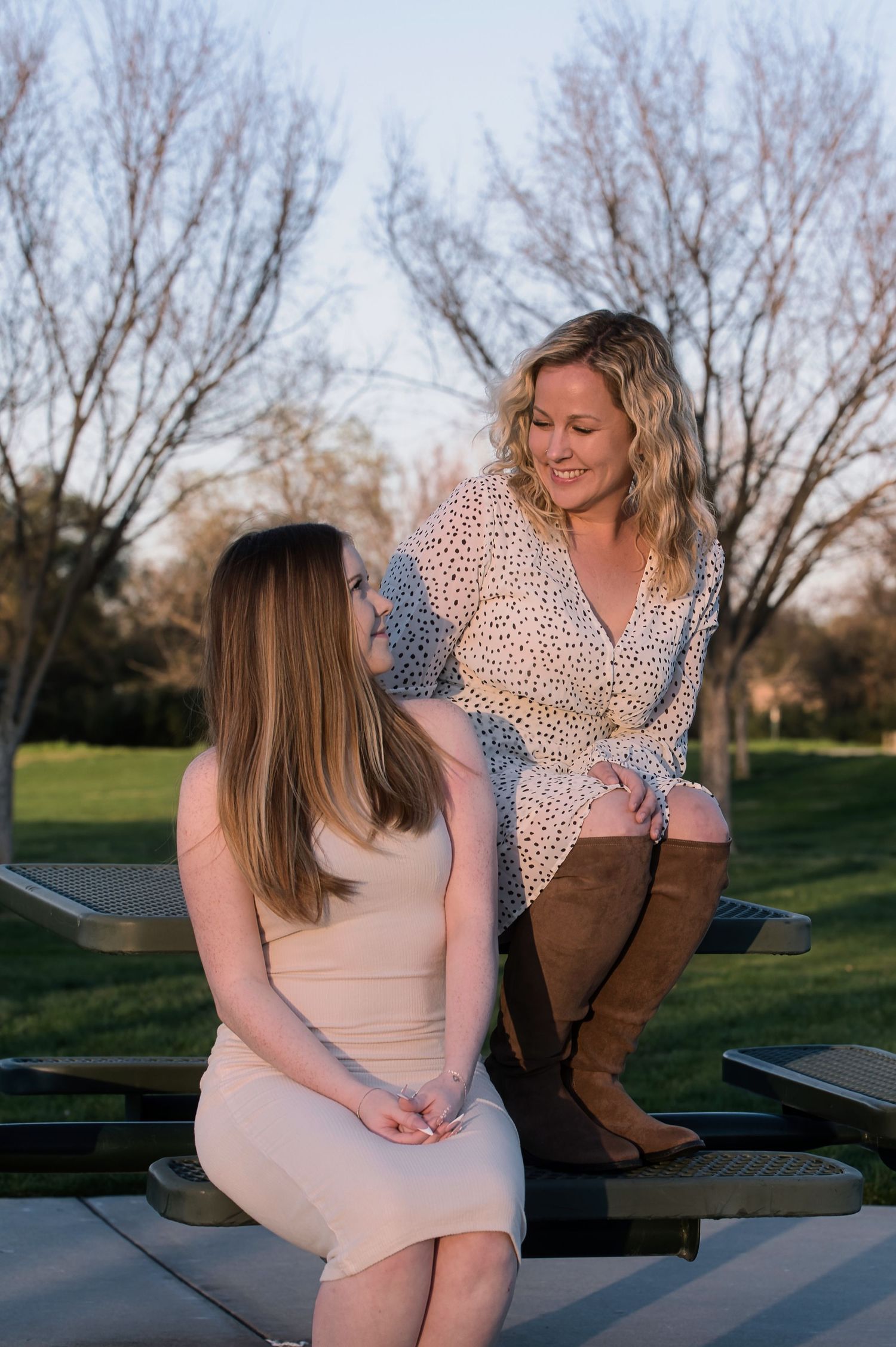 Two women share a warm moment seated on outdoor furniture in a park at golden hour.