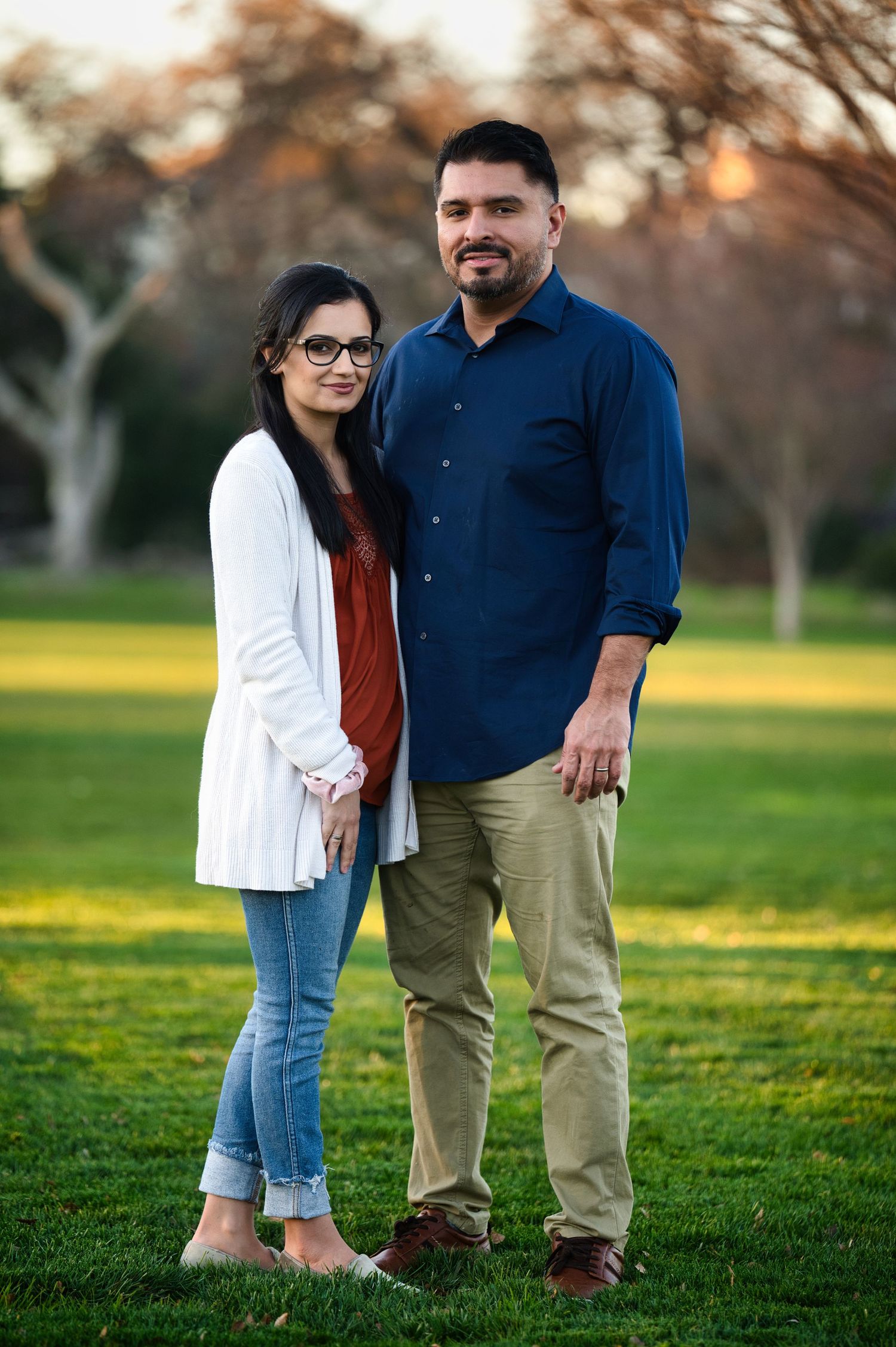 Couple standing together in park, woman in white cardigan and man in navy shirt.