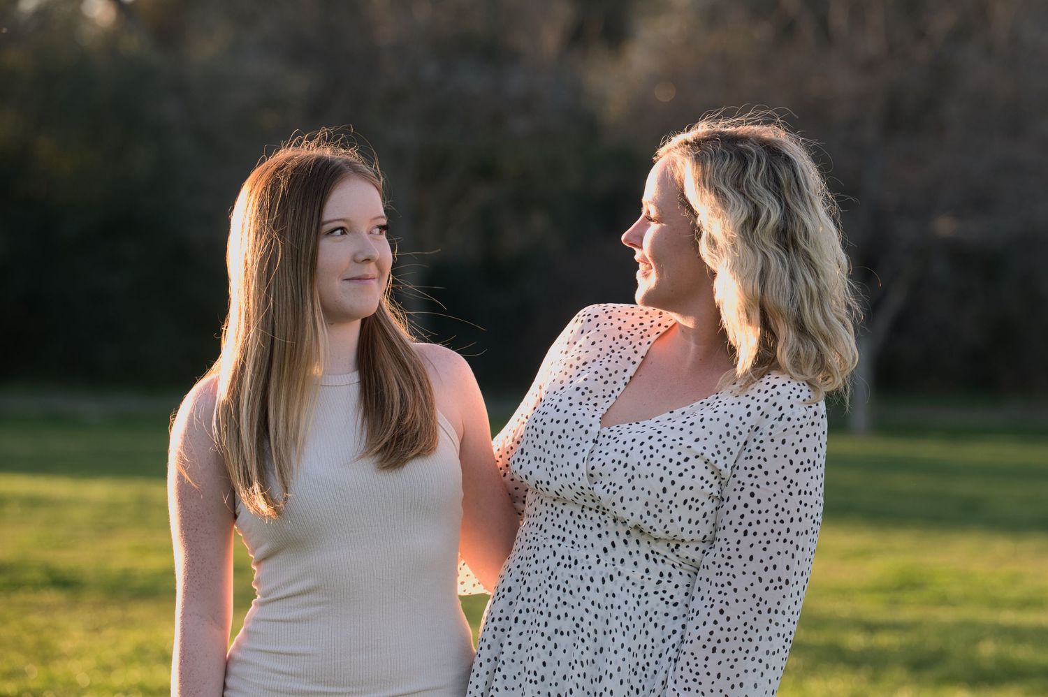 Two women laugh together in a golden-hour lit park, sharing a joyful moment.