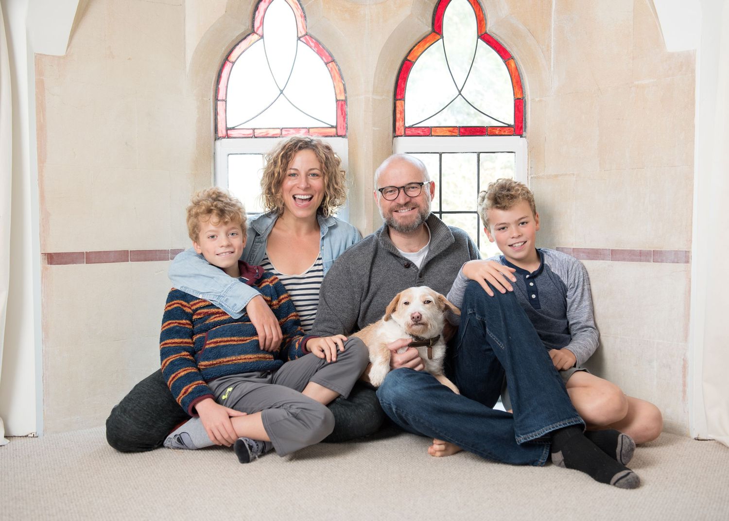 Family lying casually together on beige carpet during an indoor photoshoot.