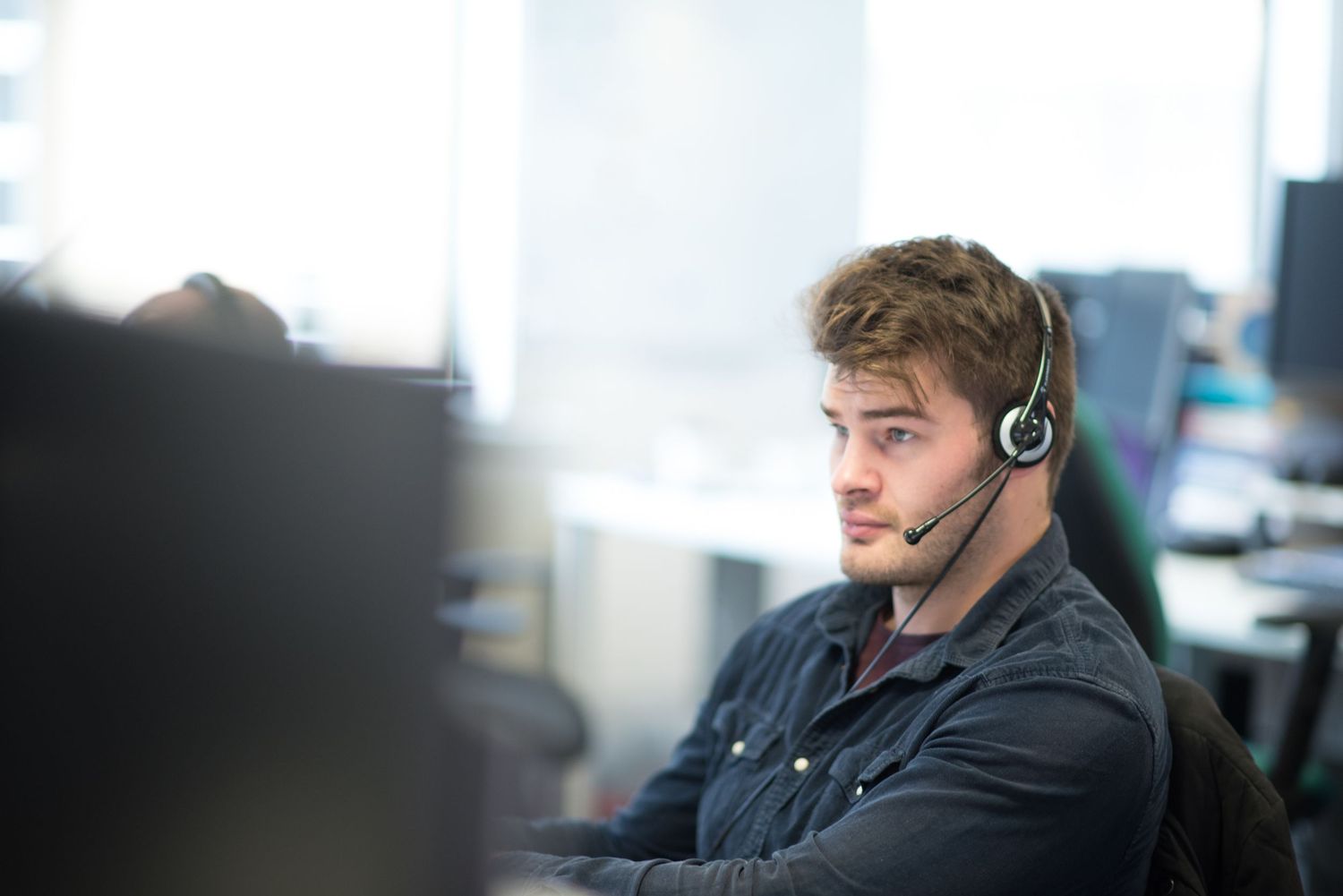 Customer service representatives wearing headsets work at their desks in a modern office environment.