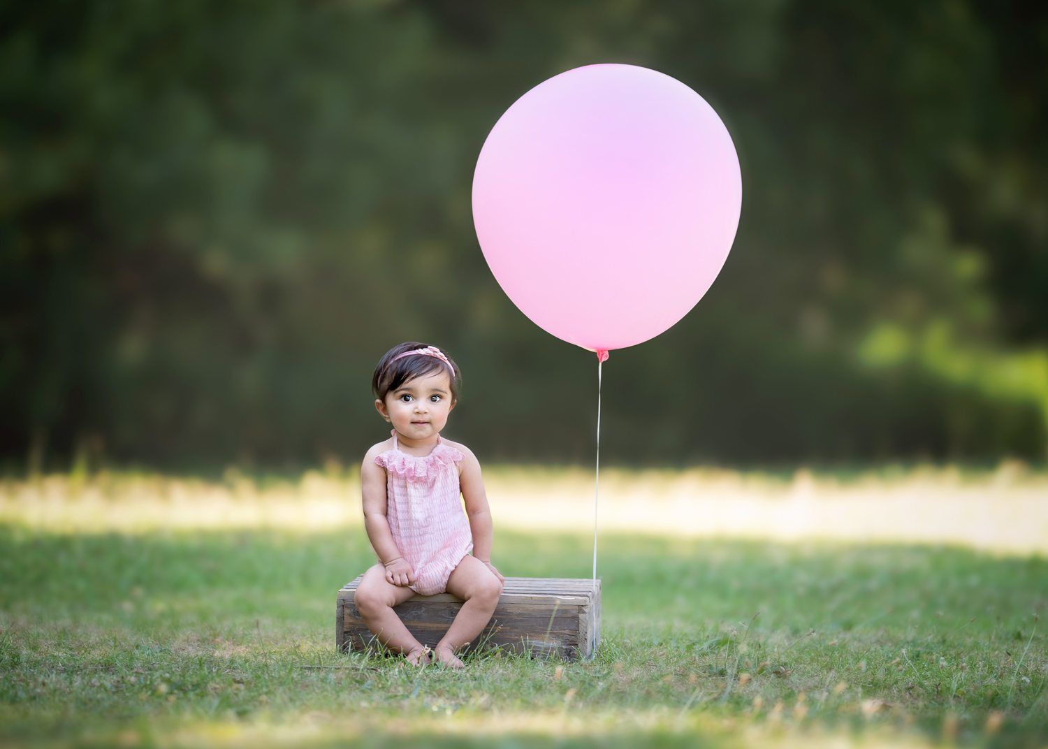 Child sitting on ground outdoors with large pink balloon.