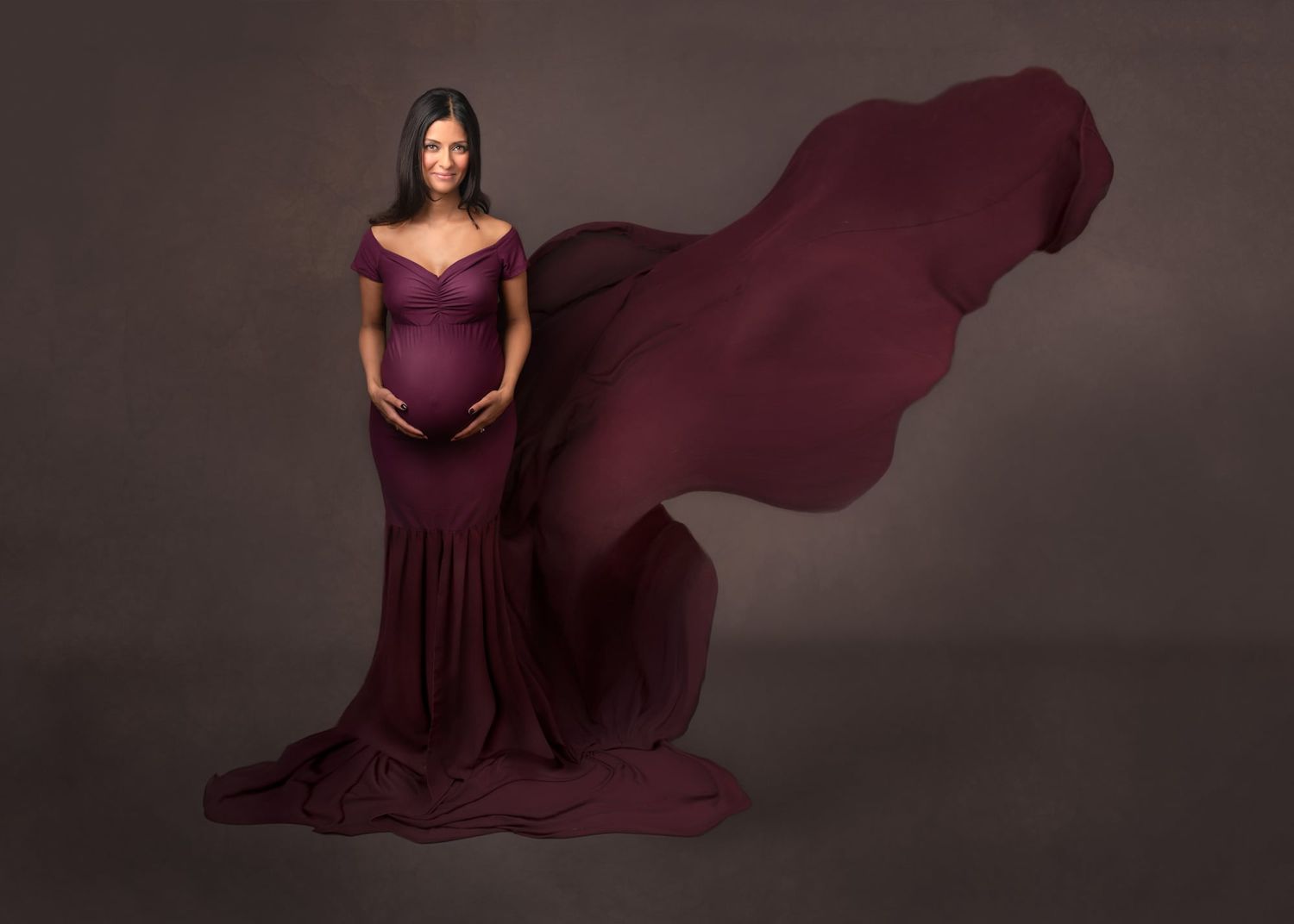 Dramatic maternity portraits with flowing burgundy fabric against neutral studio background.