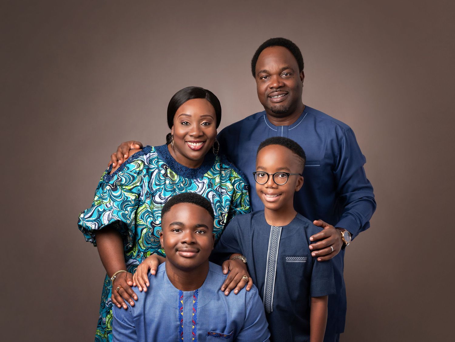 Professional studio portrait of a family in coordinating blue outfits against a brown background.