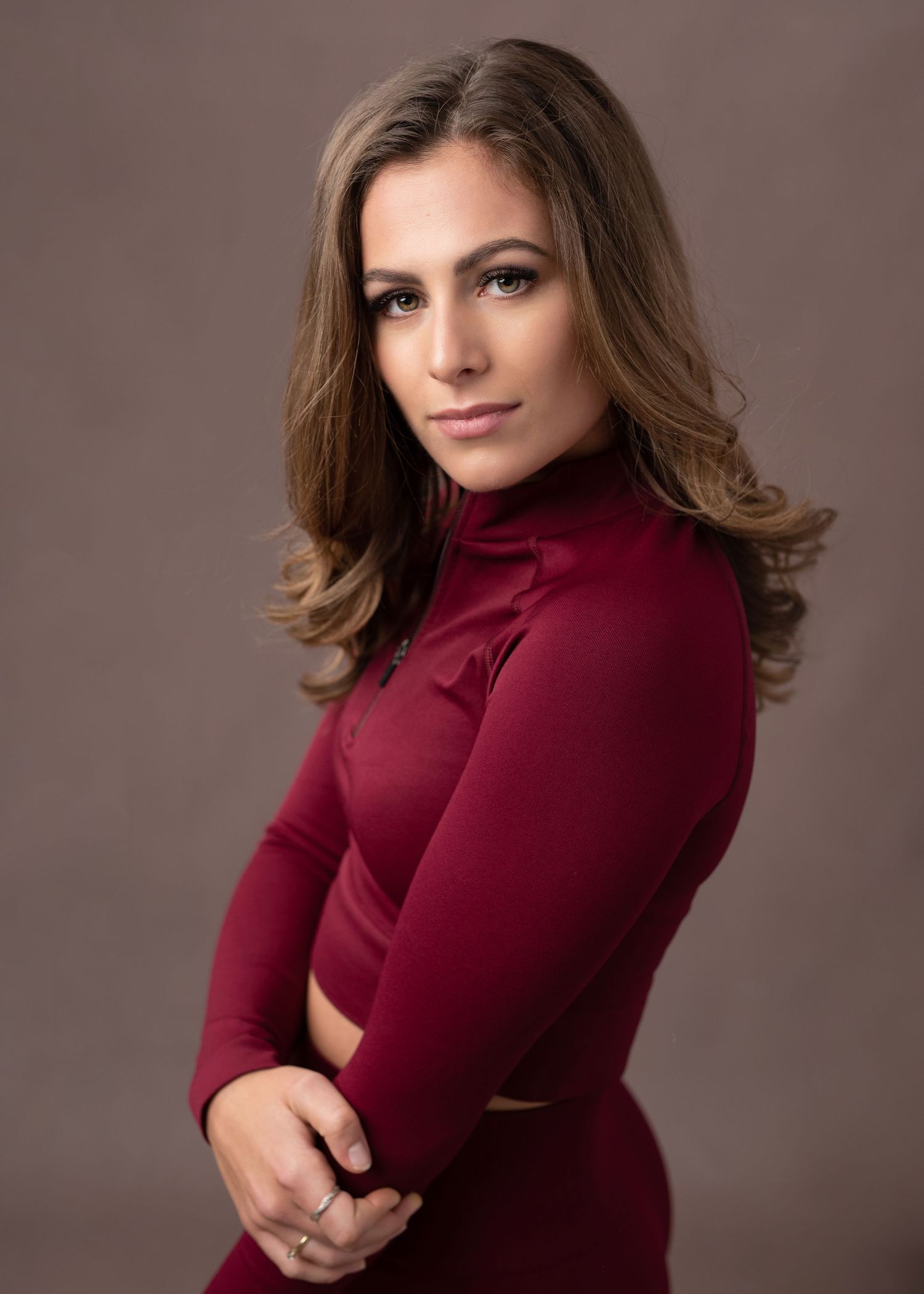 Professional portrait of a person in a burgundy turtleneck sweater against a neutral brown backdrop.