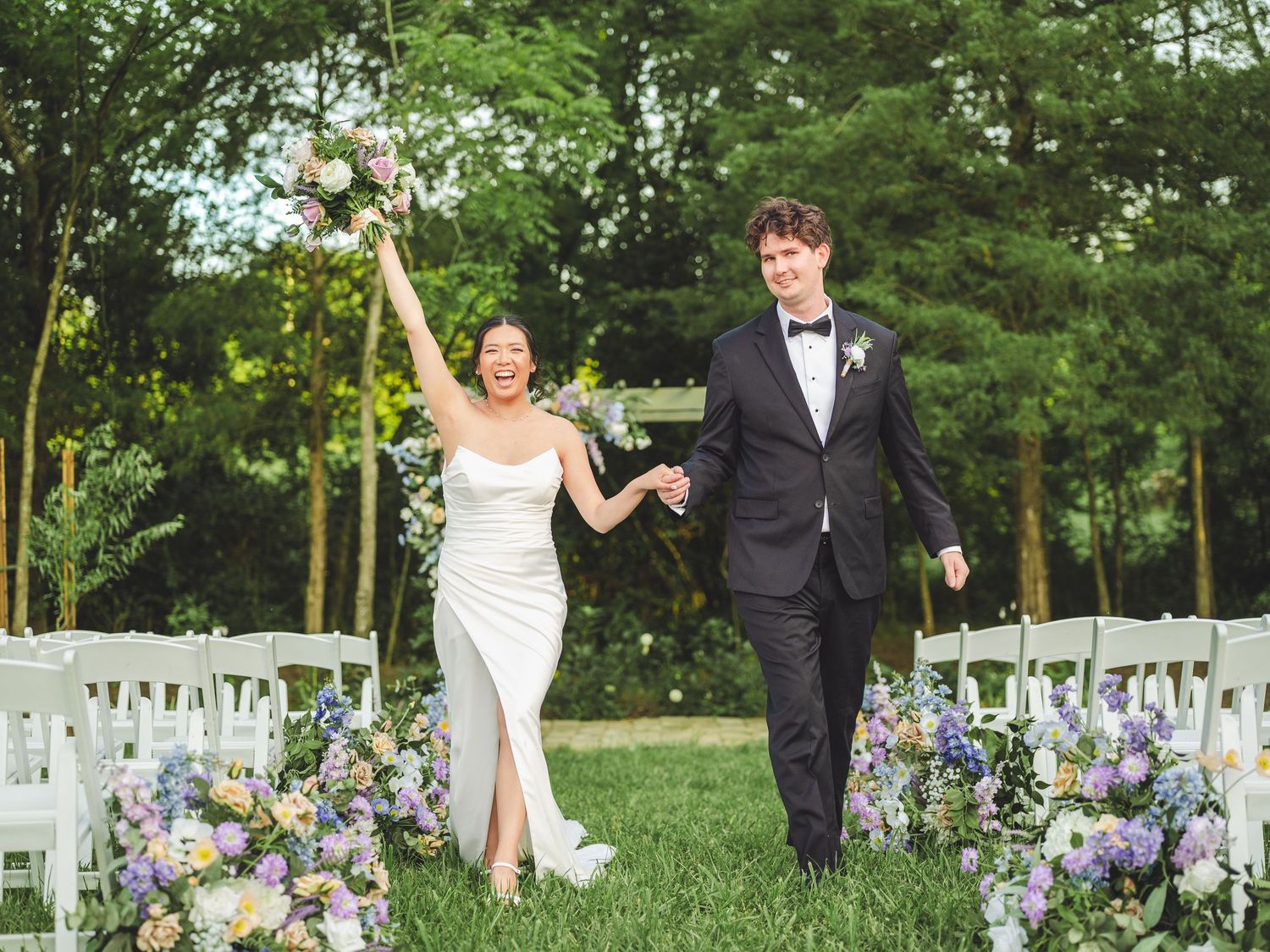 Wedding party members running joyfully through a garden setting with purple delphinium flowers lining the path.