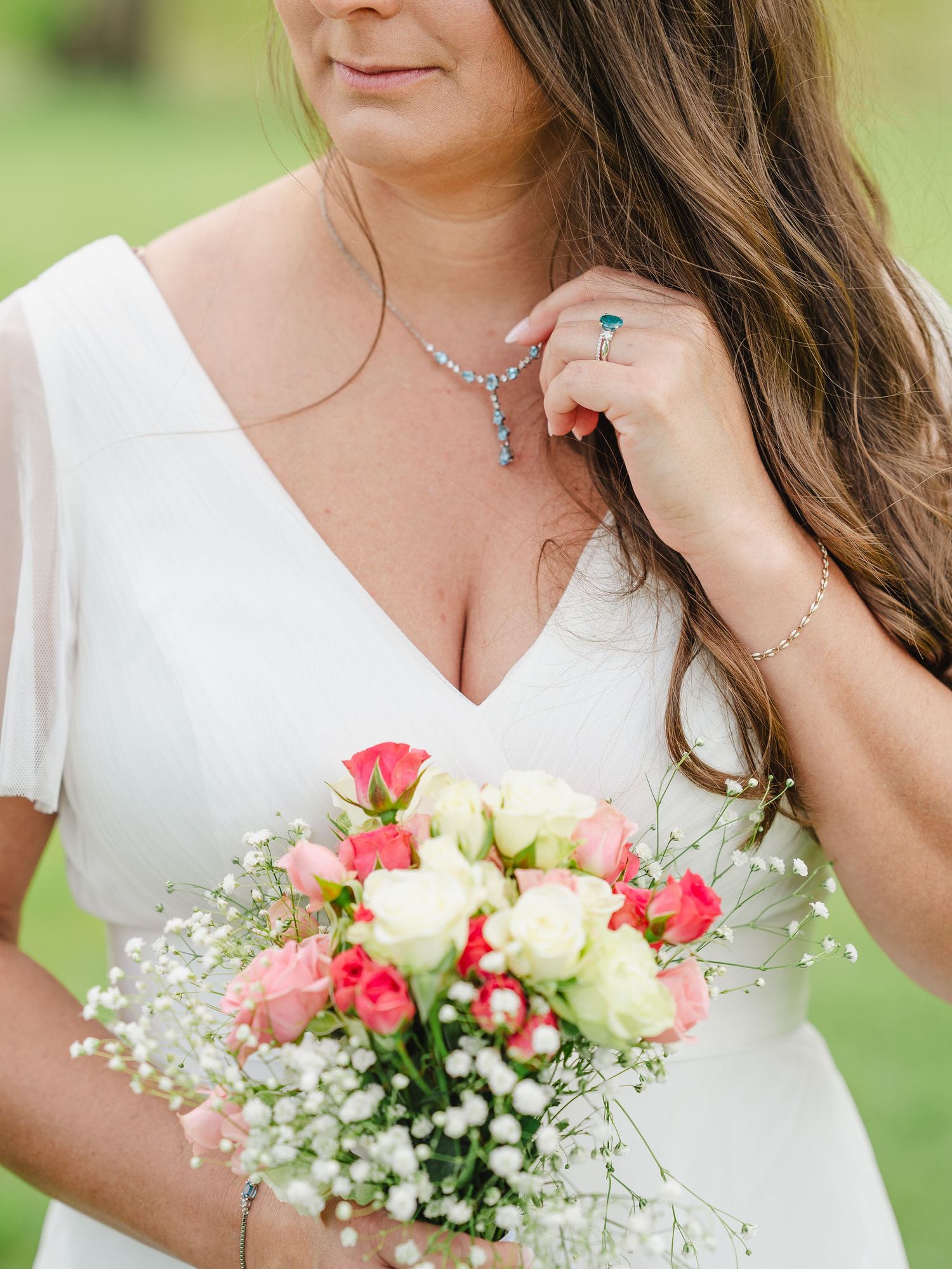 Close-up detail showing wedding flowers with pink roses and baby's breath against a white dress in natural outdoor lighting.