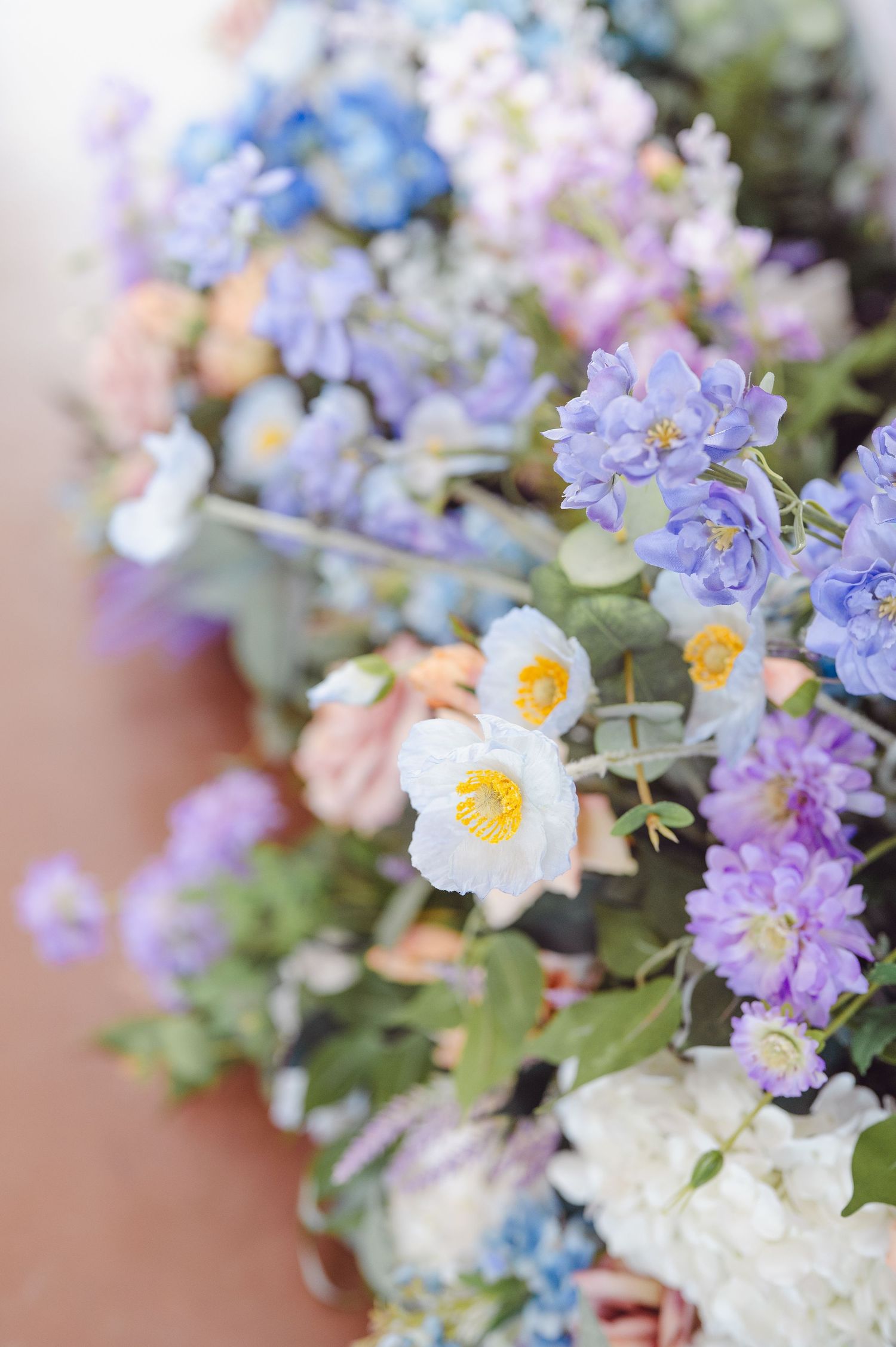 Close-up of delicate spring flower arrangement with soft blue and purple blooms mixed with white daisies in pastel tones.