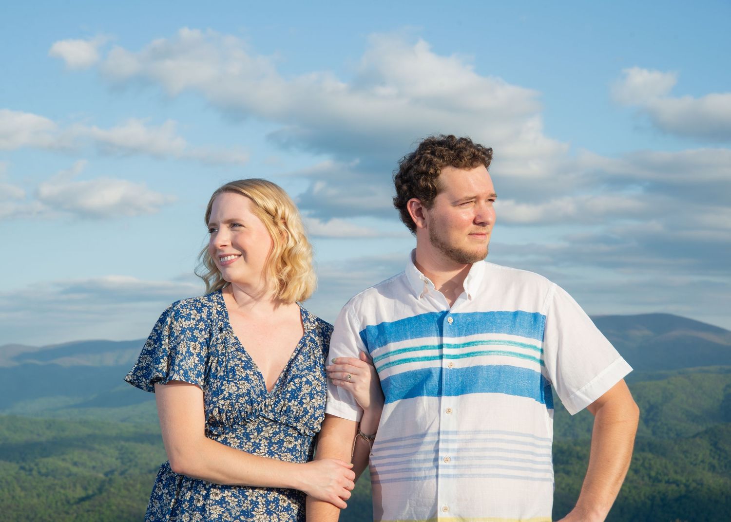 Couple enjoying scenic mountain views on summer day with blue sky and puffy white clouds in background.