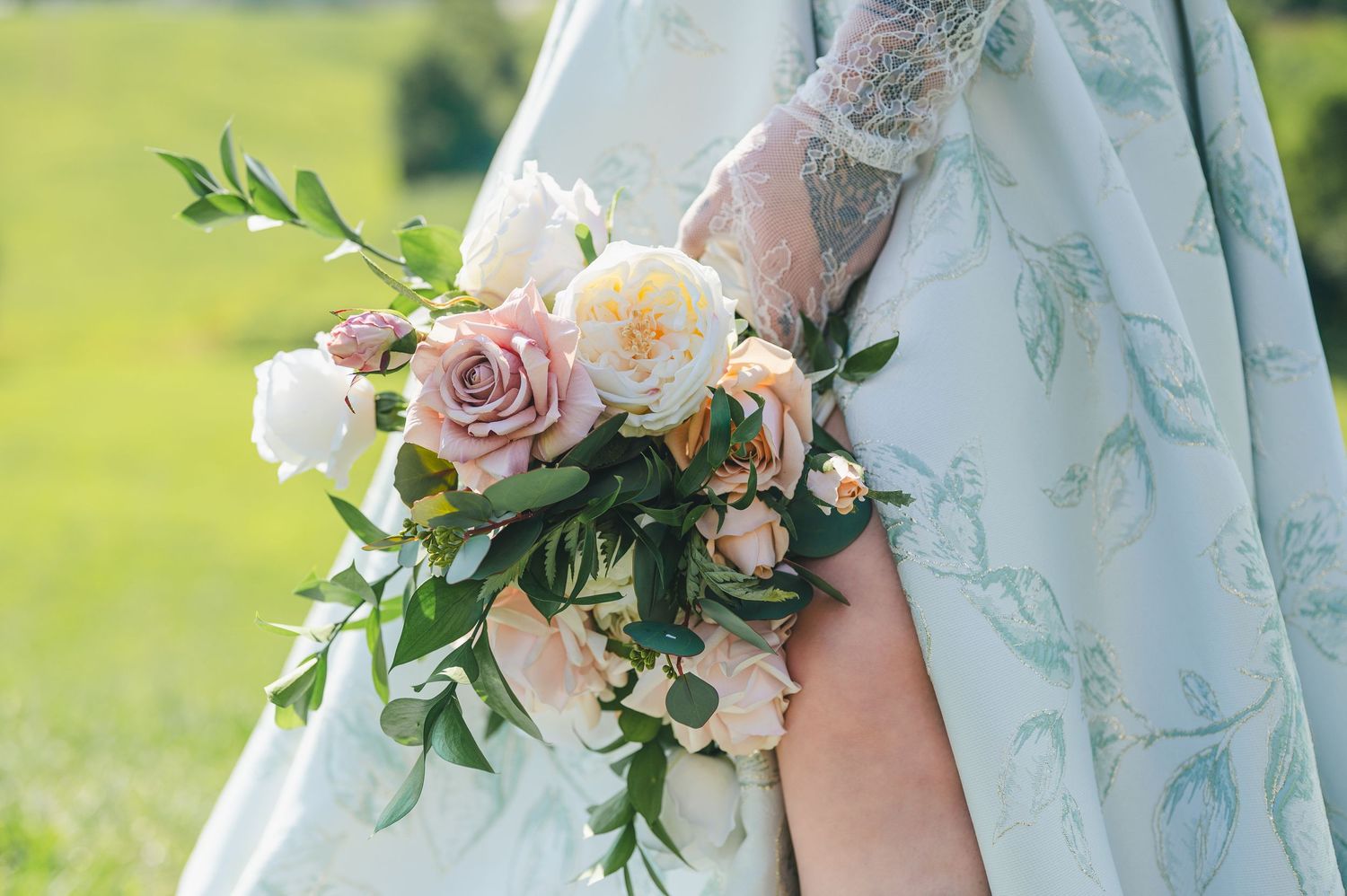 Elegant bridal bouquet with pink and cream roses rests against a mint colored dress with delicate embroidery details.