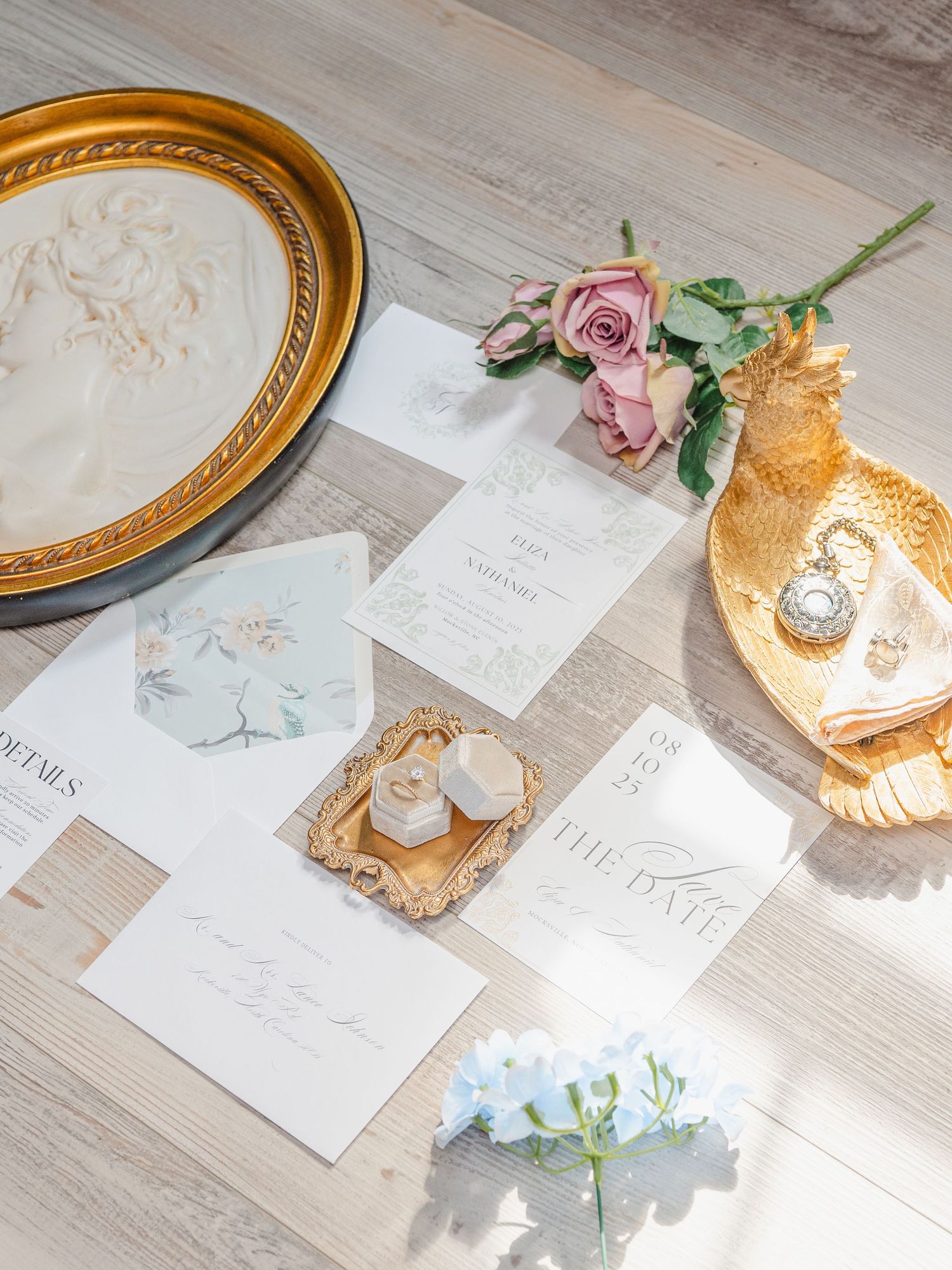 Elegant wedding stationery with gold decor plates and delicate pink roses arranged on a light wooden surface.