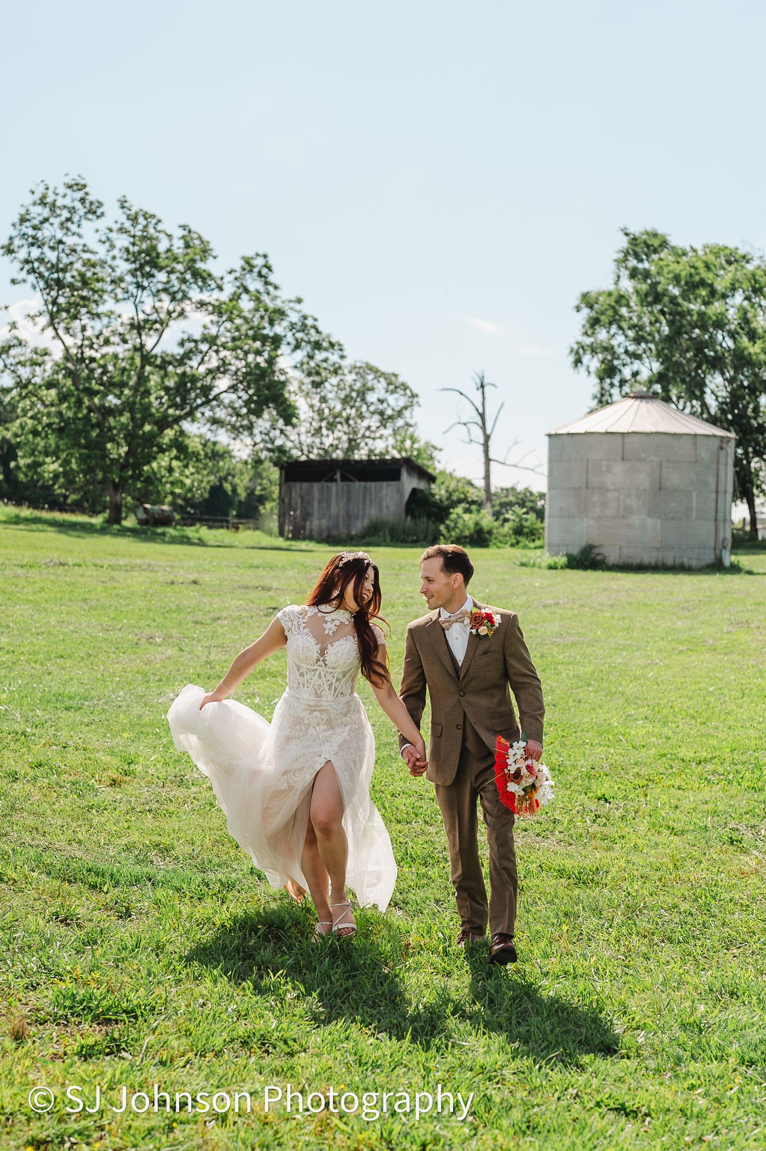 A couple walks across a sunny green hillside in North Carolina as her white wedding dress flows in the breeze.