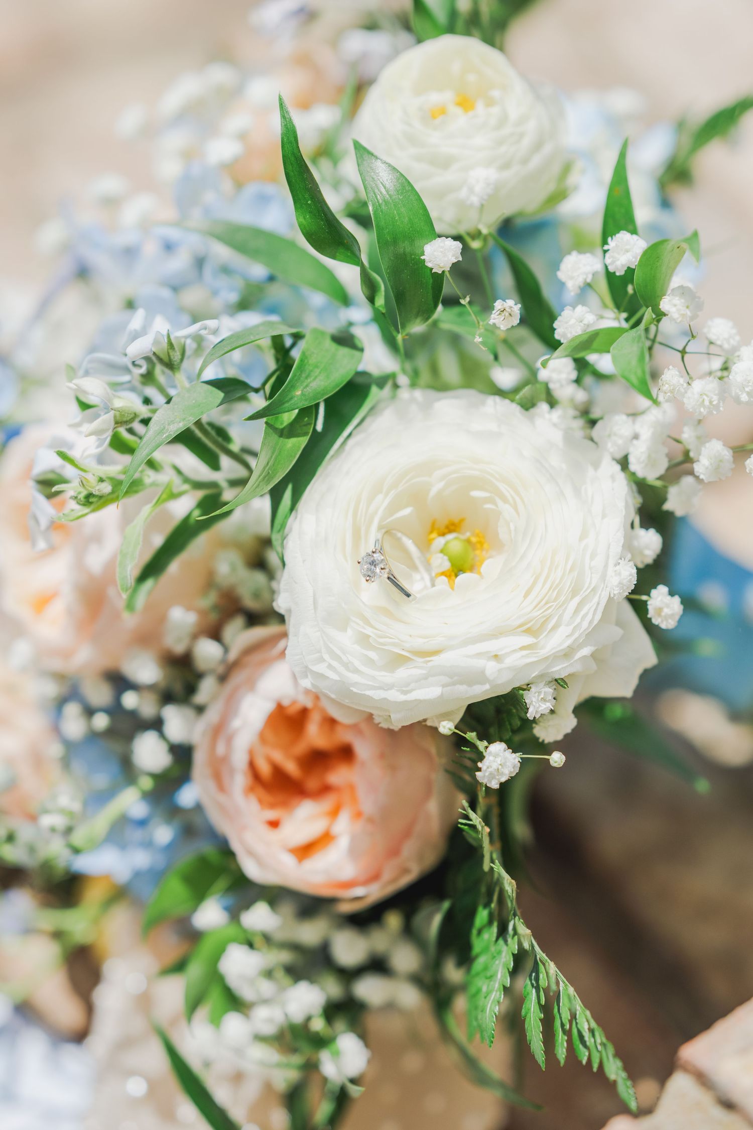 Close-up of delicate white ranunculus and peach garden roses with baby's breath in a soft spring floral arrangement.
