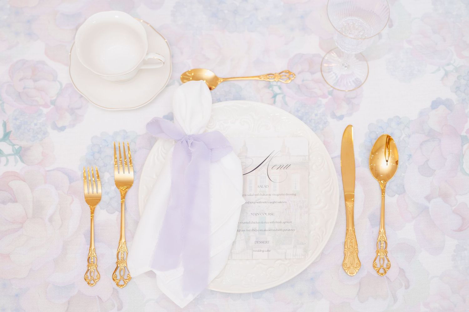 Elegant table setting with gold flatware, white plate, and menu card on light marble background.