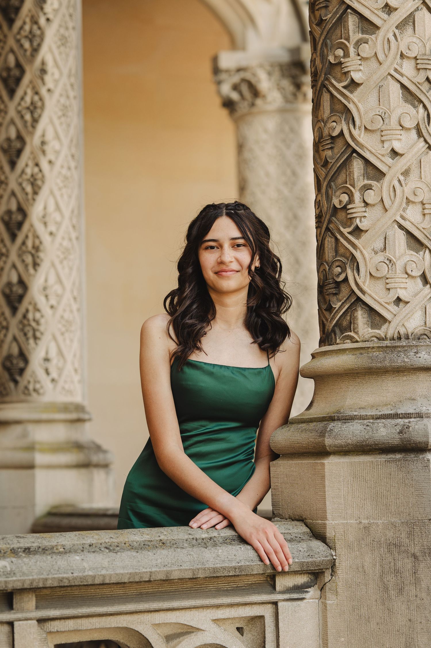 Young woman in green satin dress posing by ornate stone columns at an elegant architectural venue.