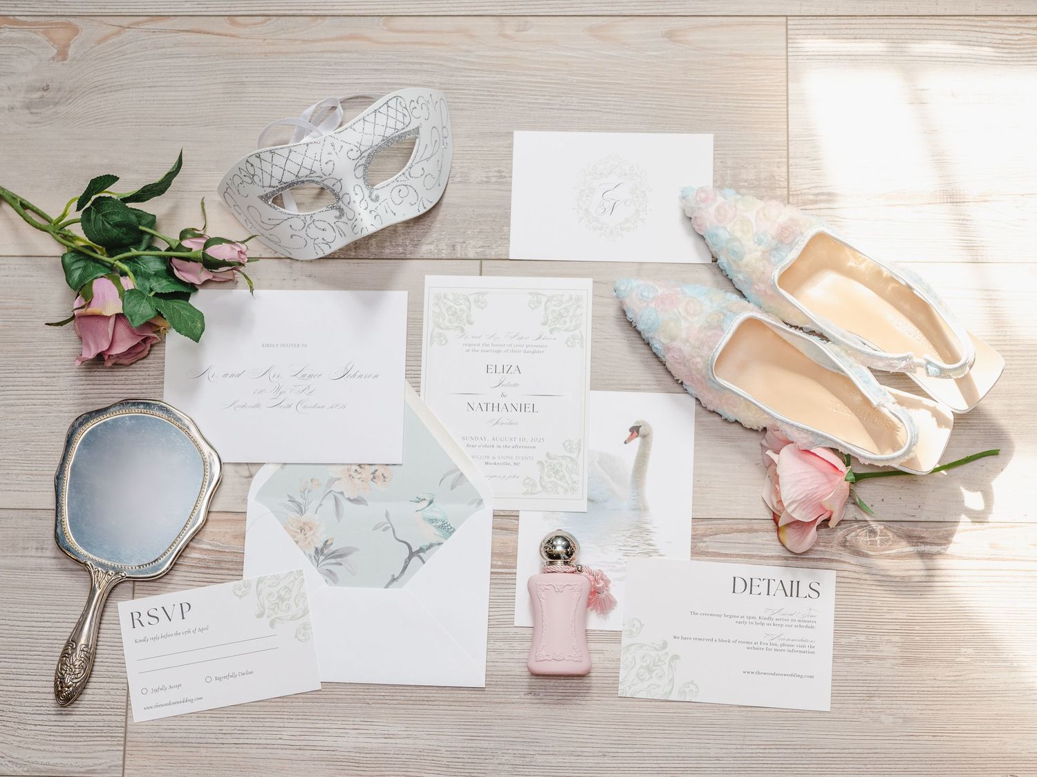 A stylish flat lay of wedding stationery with floral elements and soft pink accents on a light wood surface.