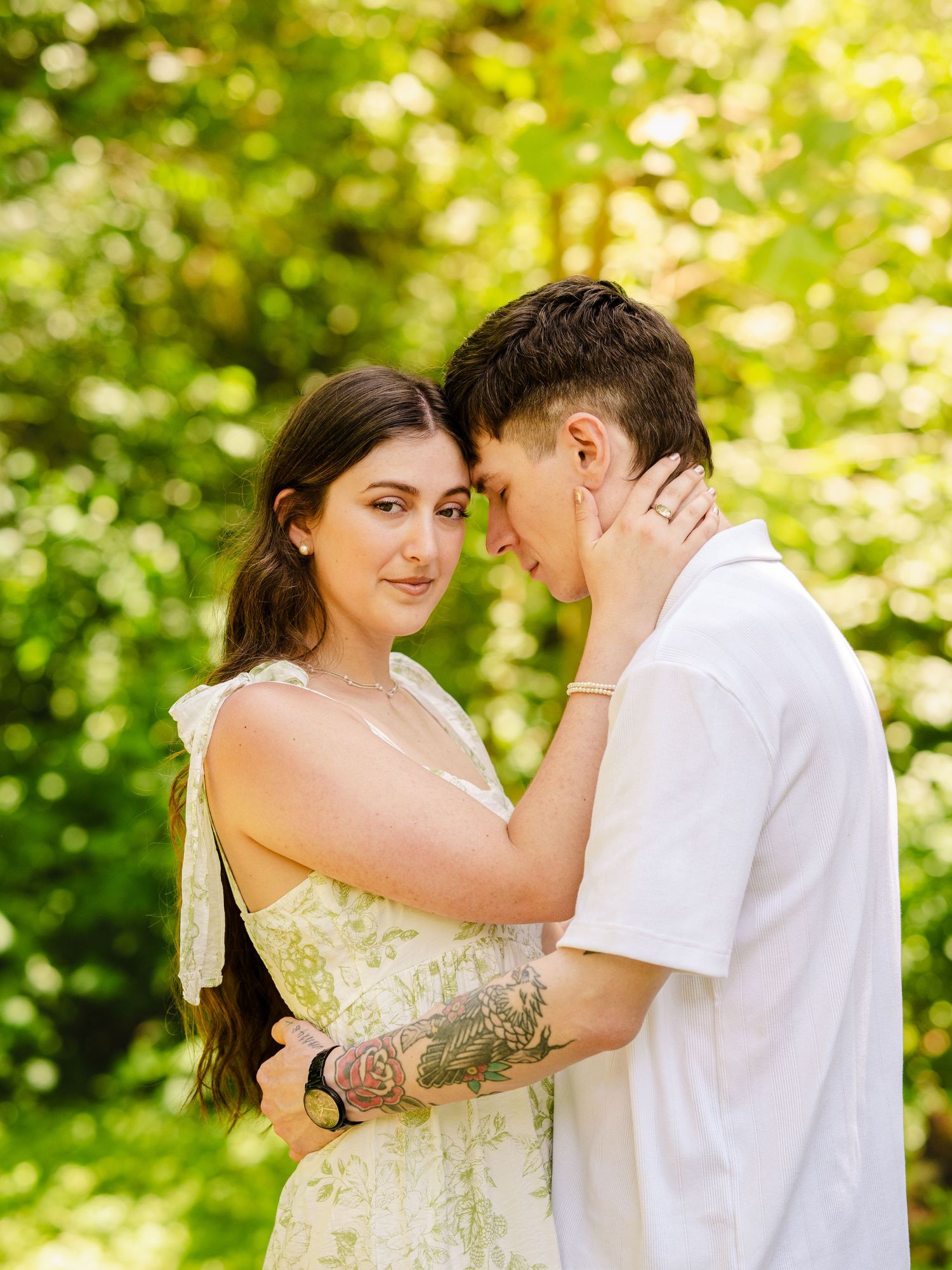 A romantic couple shares a tender moment together in a sunlit garden in North Carolina with lush green foliage in the background.