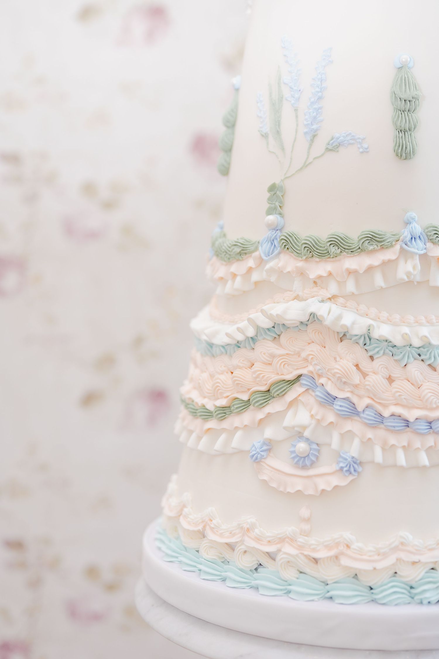 Delicate pastel wedding cake decorated with ruffled layers, soft peach tones and light blue floral accents.